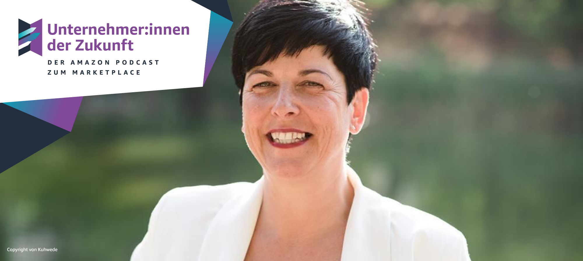 Eine Frau mit kurzen schwarzen Haaren und einer weißen Bluse lacht in die Kamera.
