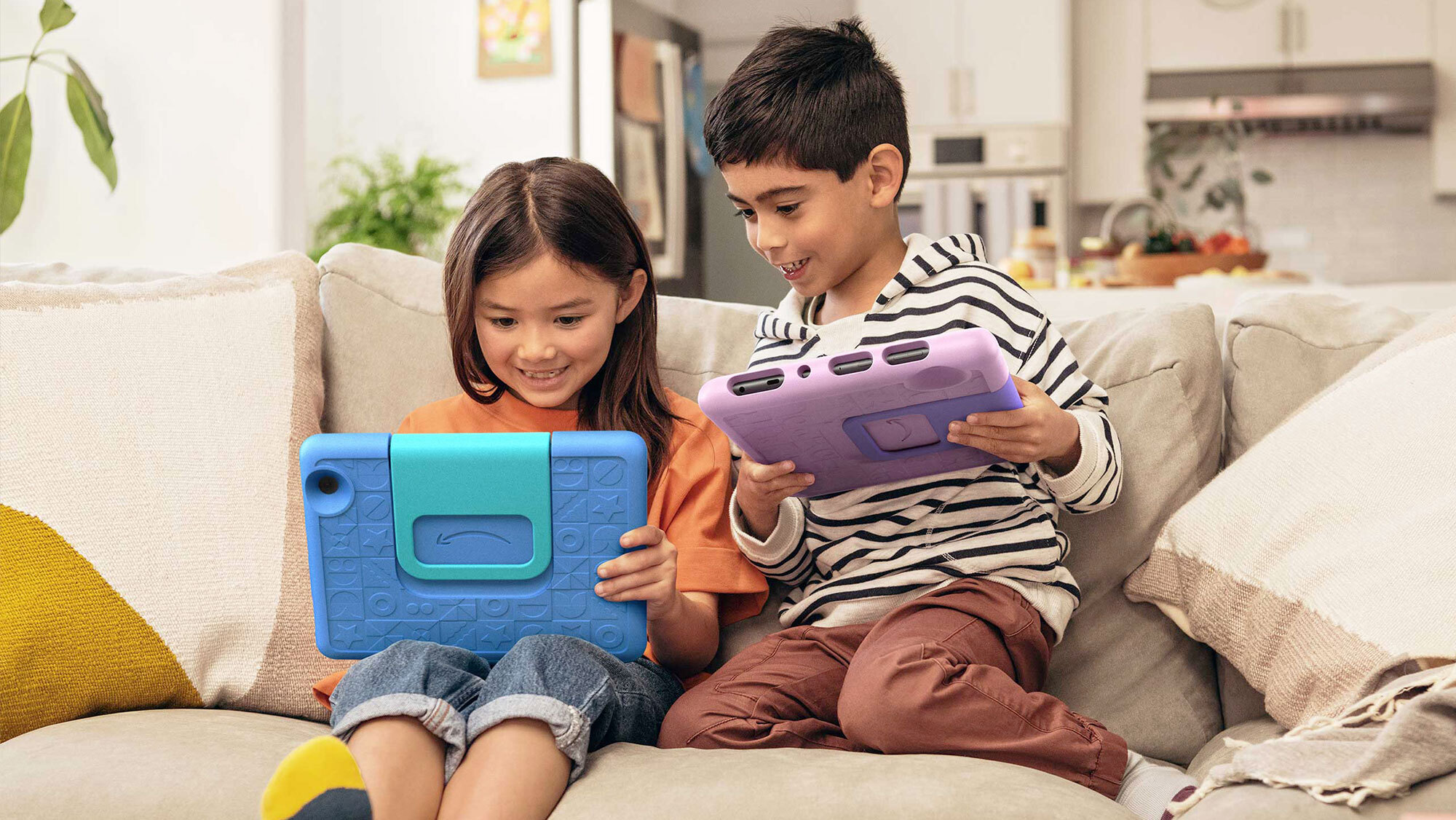 An image of two children using their Amazon tablets while sitting on the sofa. 