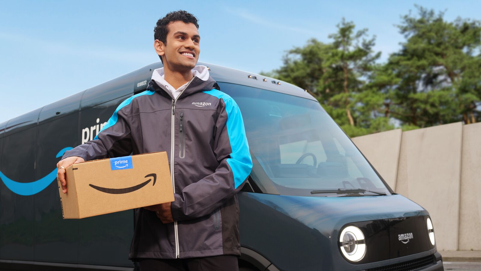 Amazon employee in branded jacket carrying package beside delivery van