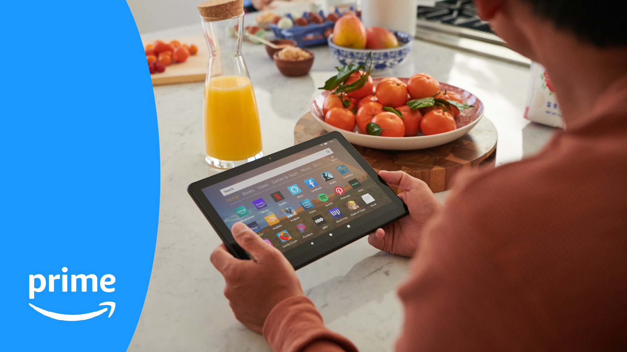 A man sits at a kitchen counter looking at his Fire Tablet, with orange juice and a bowl of tomatoes right in front of him.