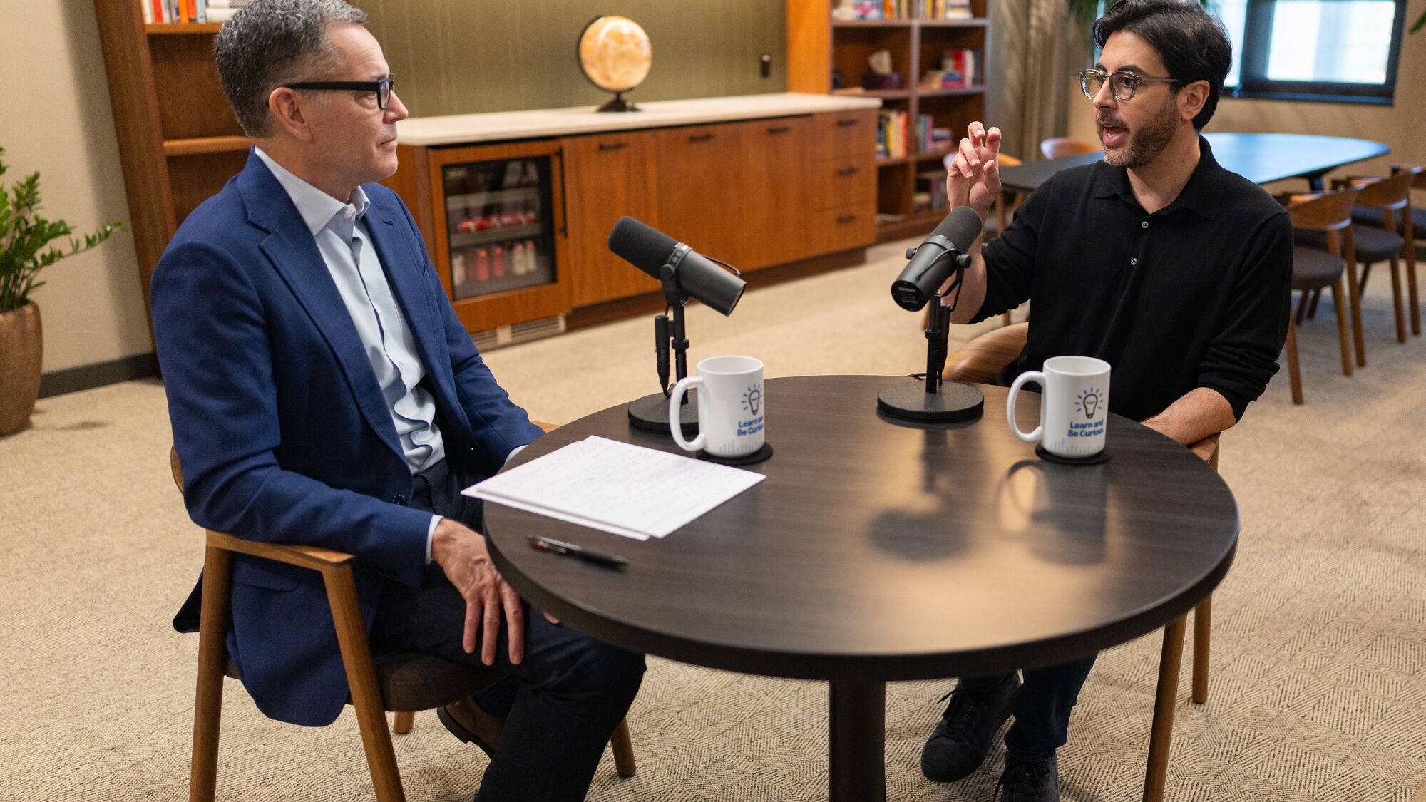 Amazon CEO of Worldwide Stores Doug Herrington interviews Alessandro Carbone in modern office setting with wooden furniture and bookshelves in background