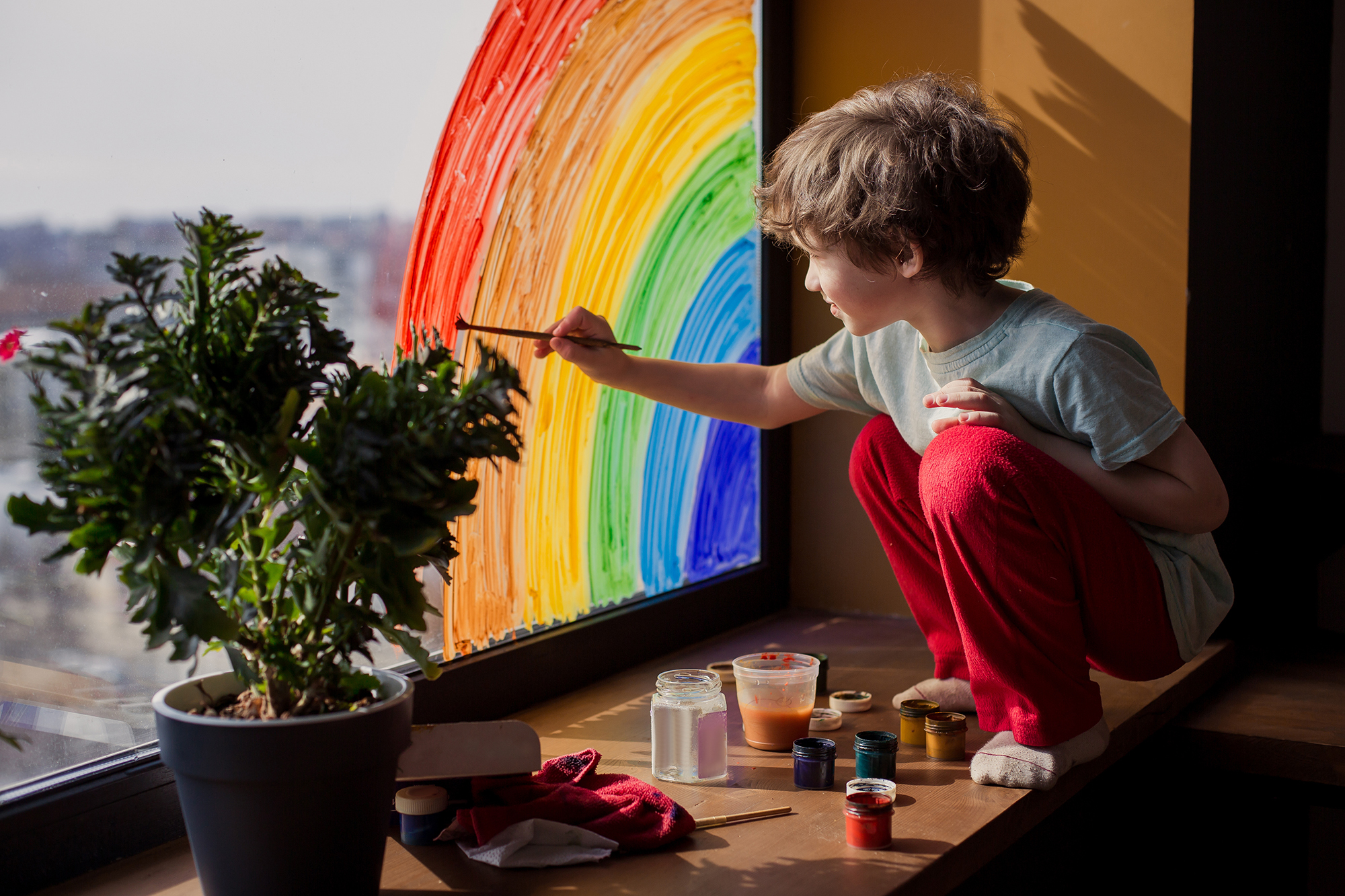 A child placing homemade rainbows in the window of their home, during COVID-19 pandemic.