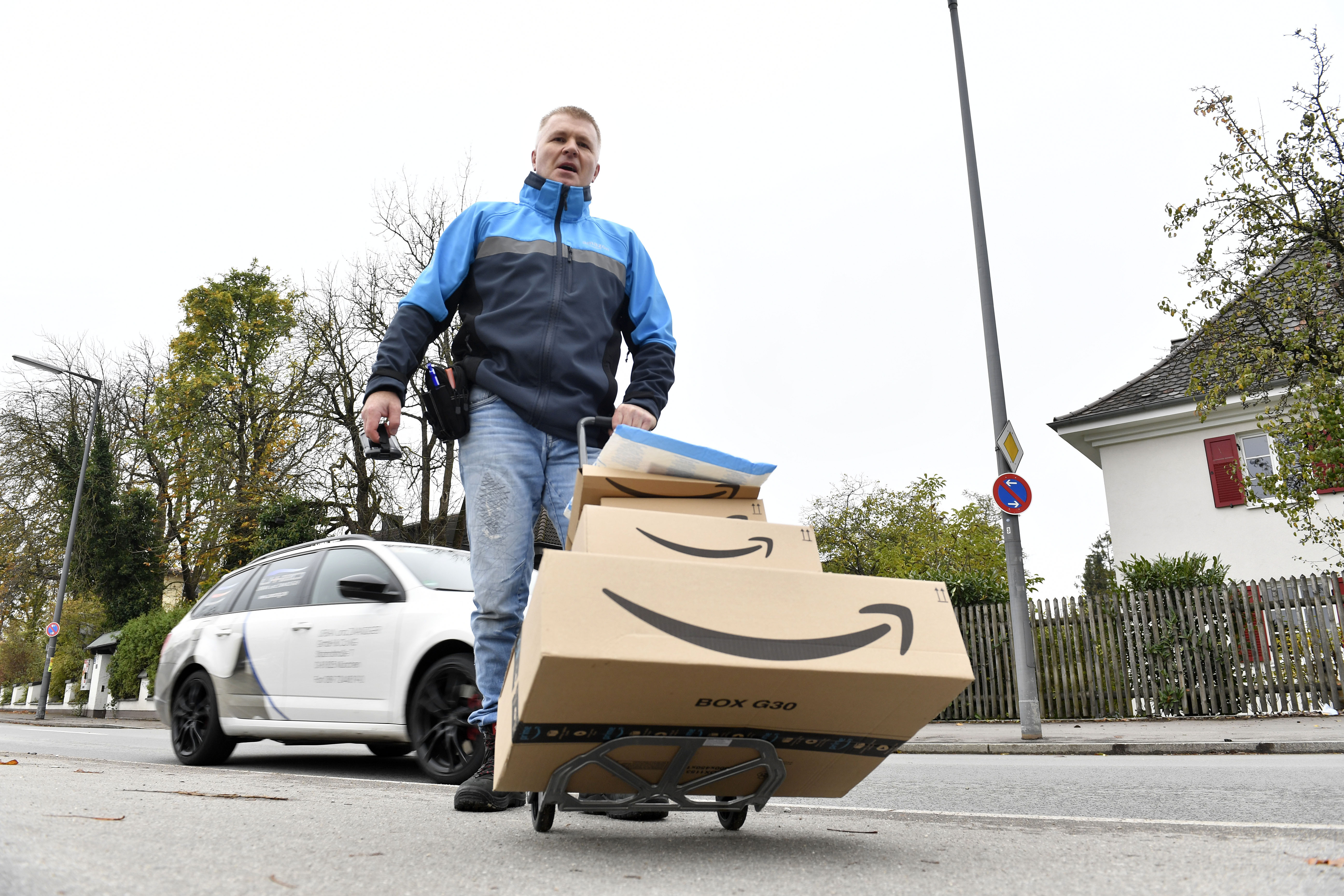 Ein Amazon Zusteller: Auf seiner Sackkarre sind mehrere Amazon Pakete.