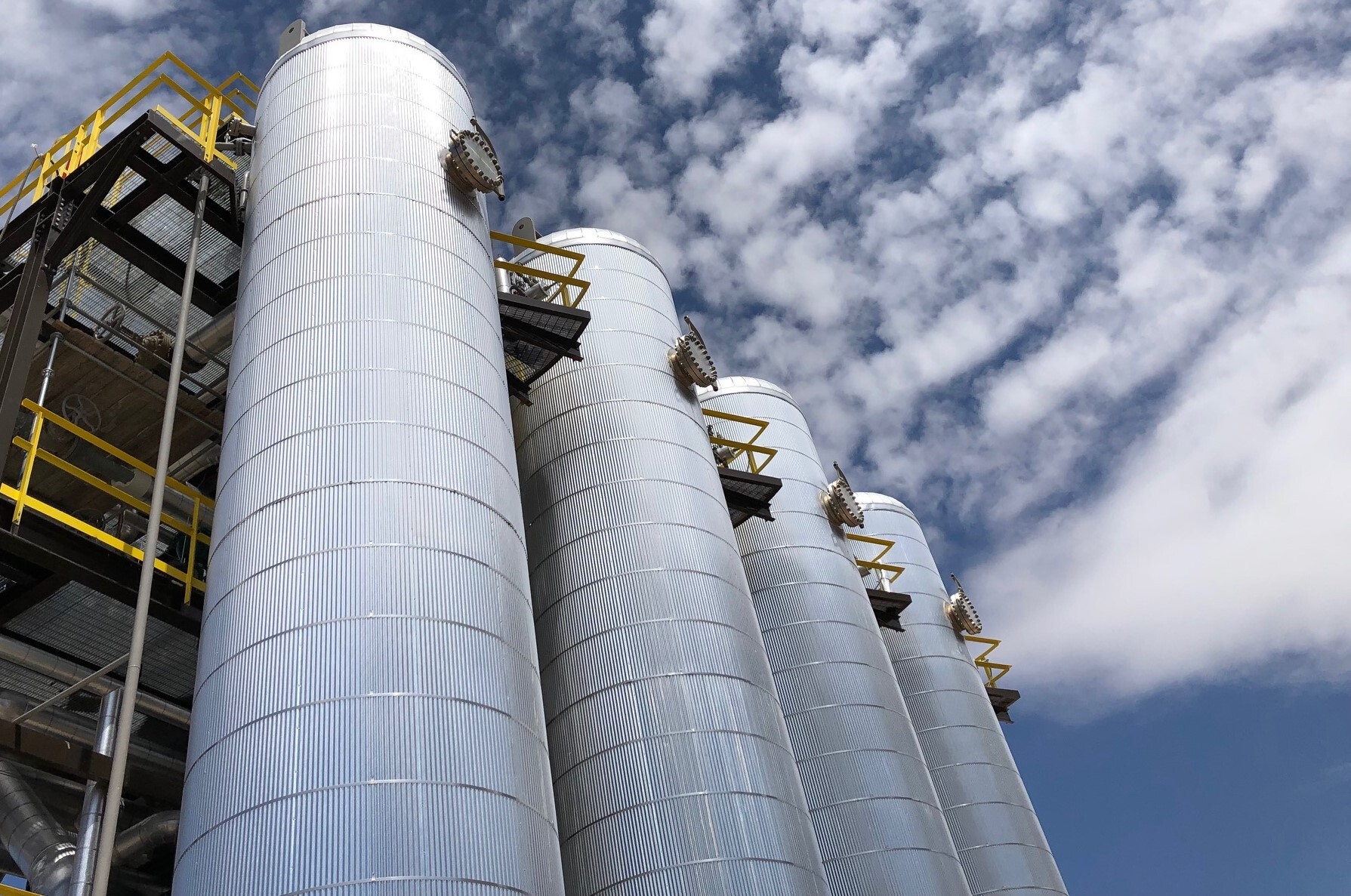 Four metal cylindrical structures shown against a blue sky with clouds.