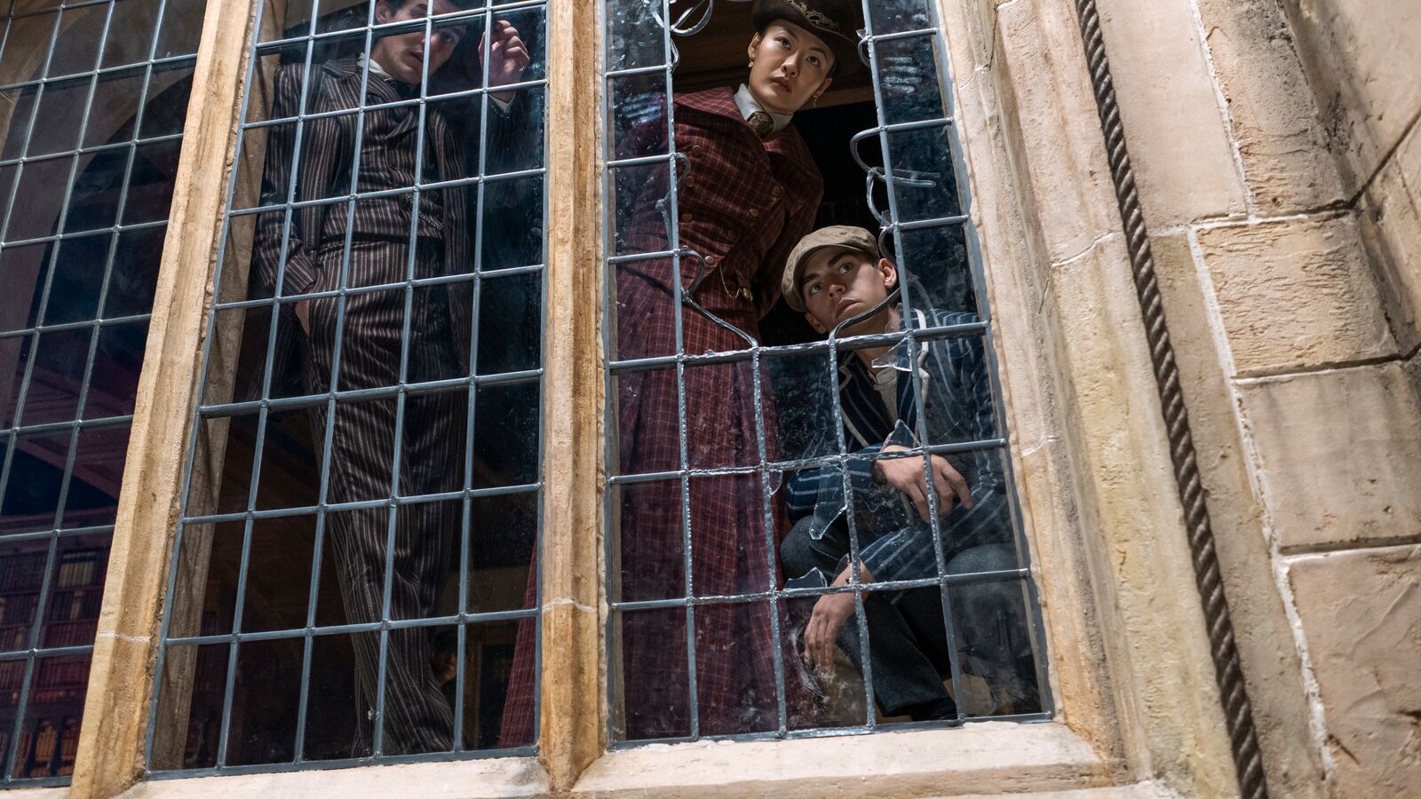 A scene from Young Sherlock on Prime Video with people peering through old window with wire mesh