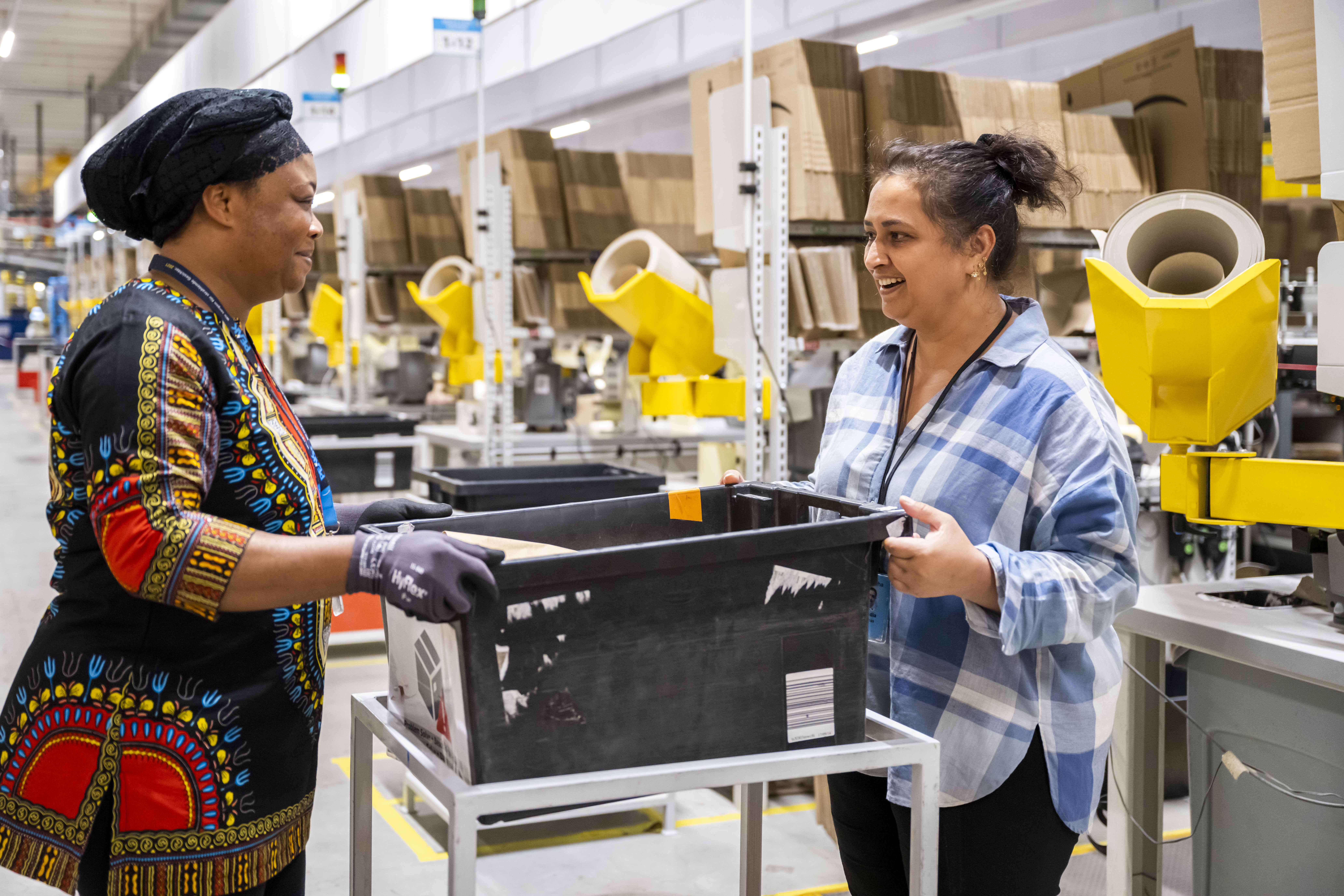 Amazon Mitarbeiter:innen, die einen schwarzen Transportbehälter anheben.
