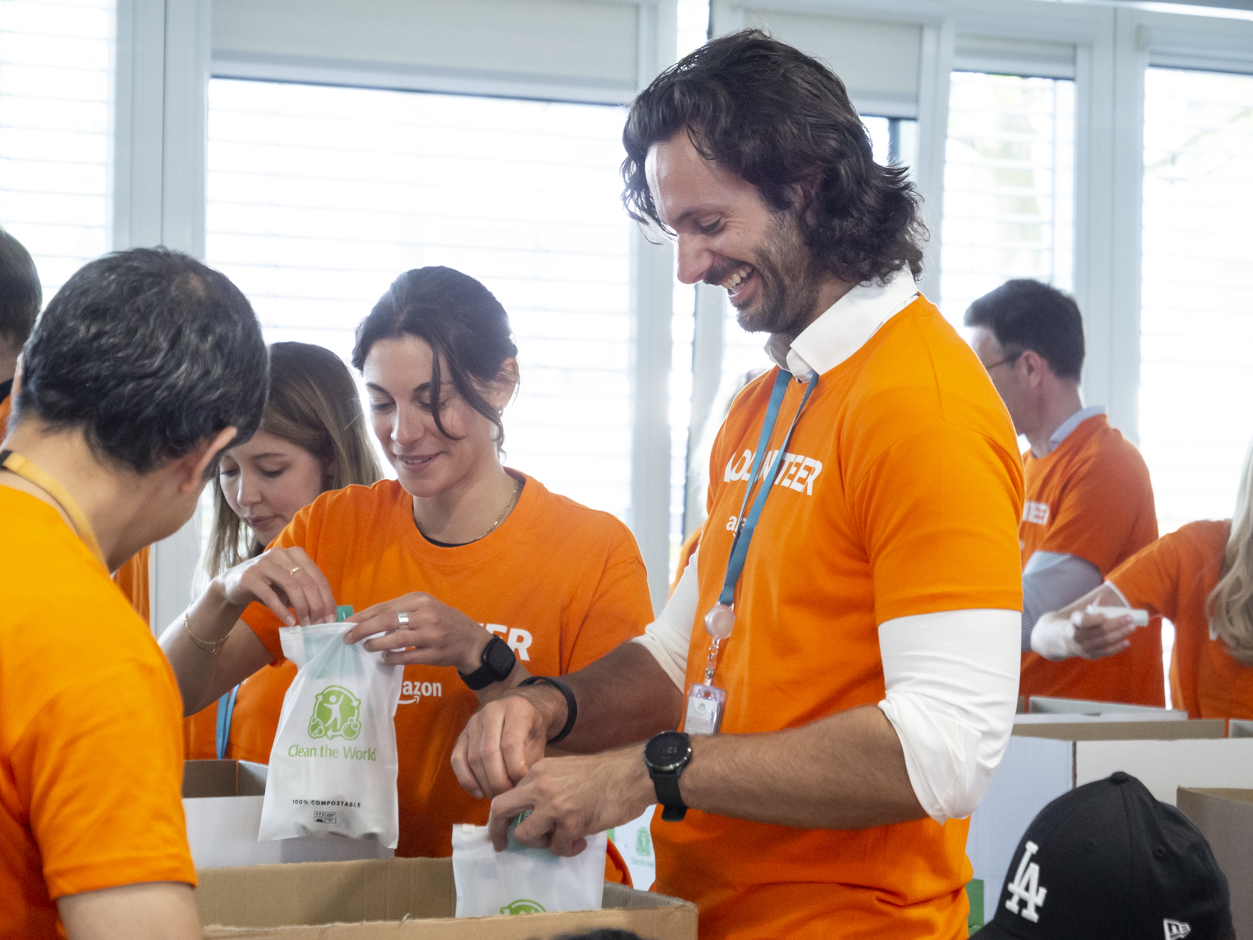 Mehrere Amazon Mitarbeiter:innen in orangenen Volunteer T-Shirts beim Packen von Hygienesets für bedürftige Geflüchtete.