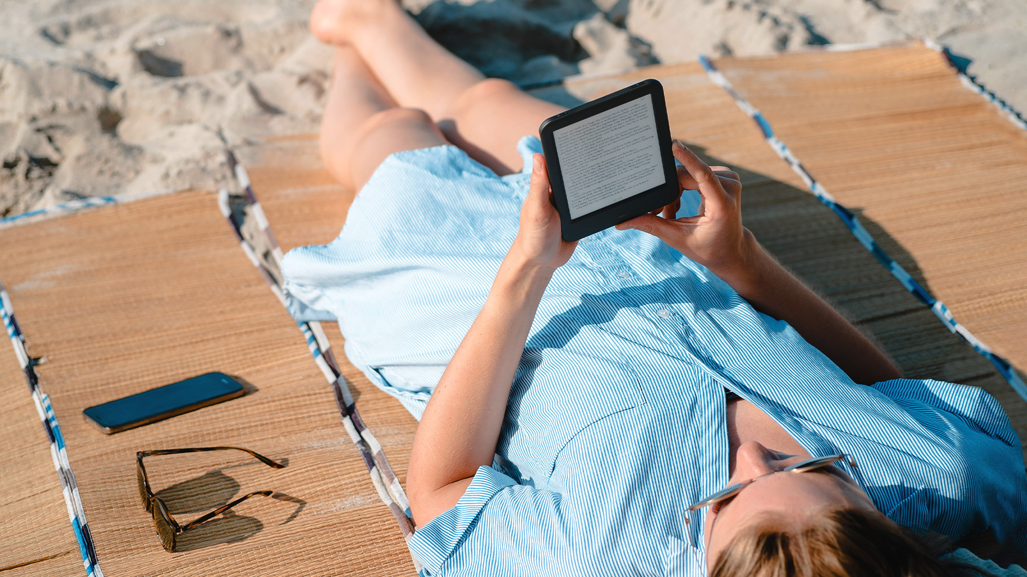 Eine Person, die am Strand liegt und auf ihrem Kindle-Gerät liest