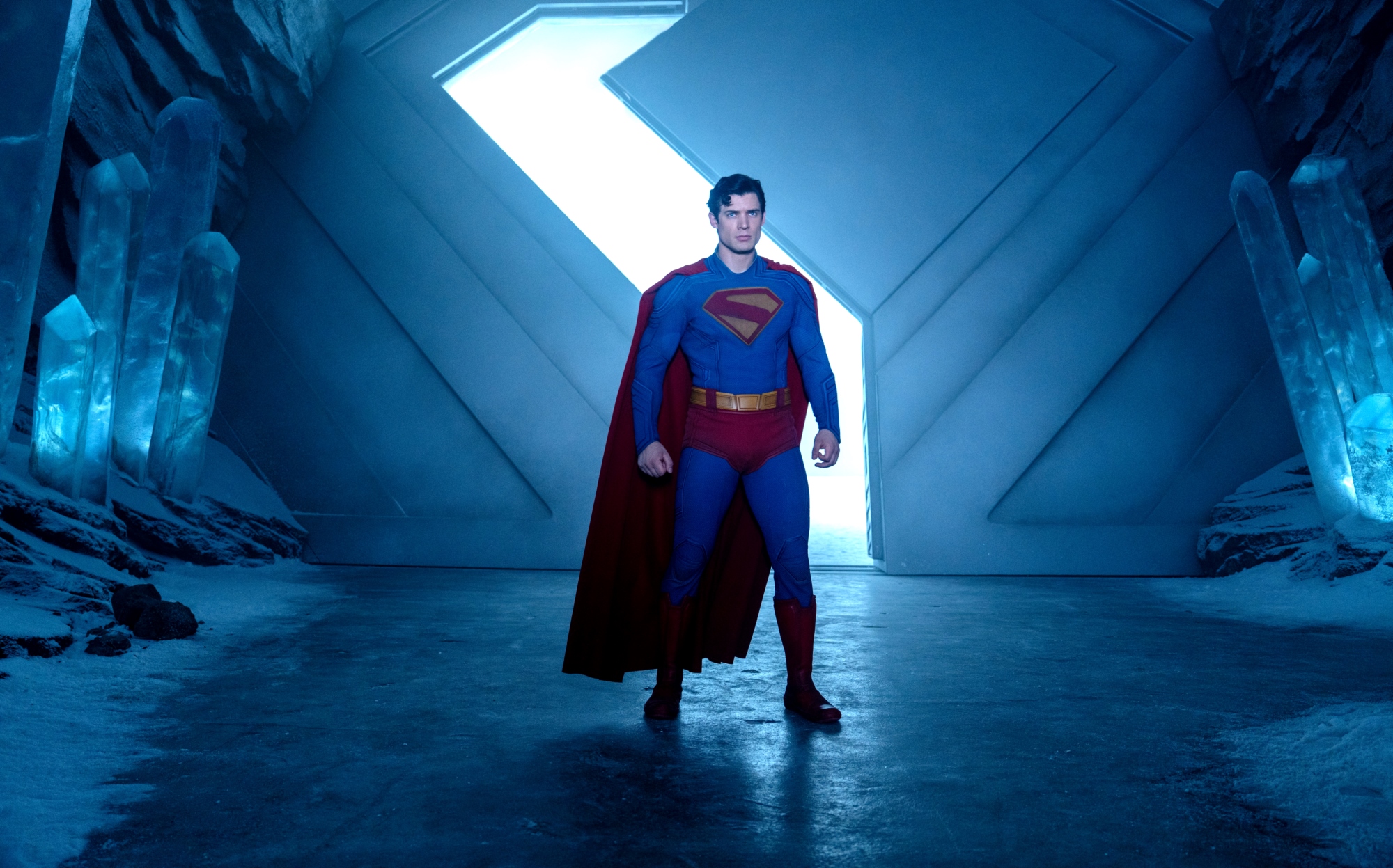 Superman stands heroically in a futuristic blue-lit corridor