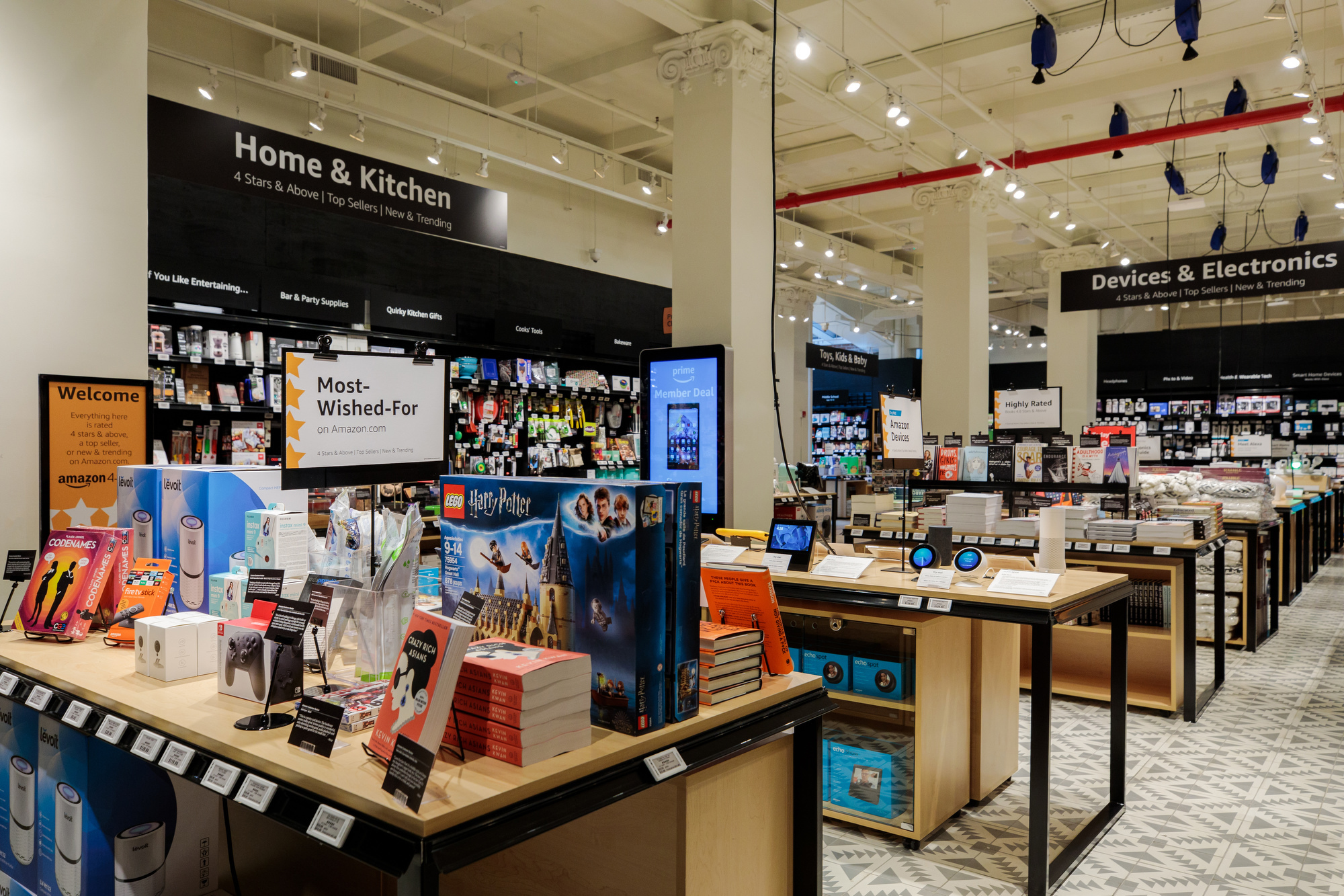 The view inside Amazon 4-star store. Tables are stacked with books, toys, devices, kitchen implements, and cookbooks.  "Home & Kitchen," "Devices & Electronics," and Toys, Kids & Baby section signage is visible.