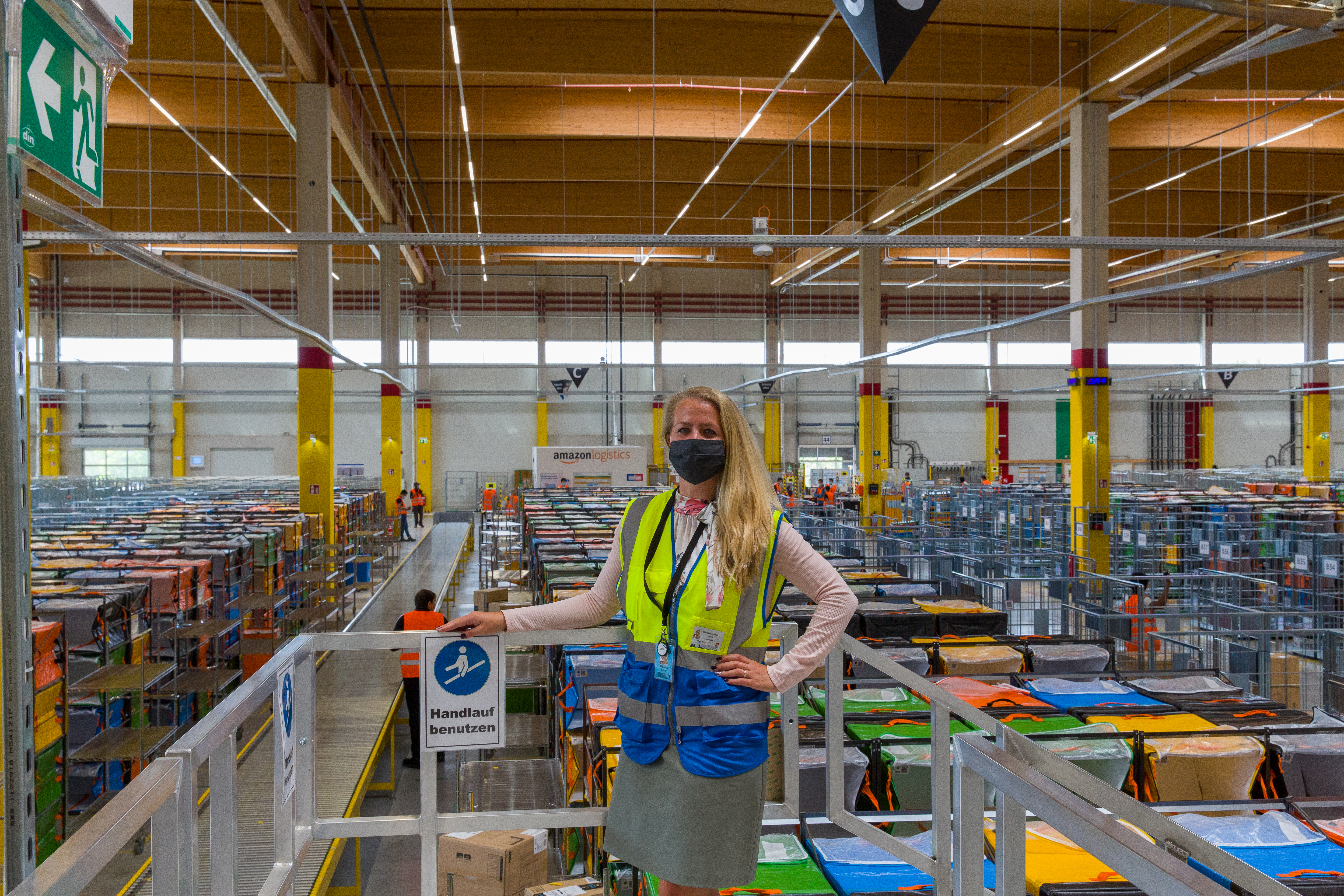 Eine blonde Frau mit Atemschutzmaske steht in einer Logistikhalle