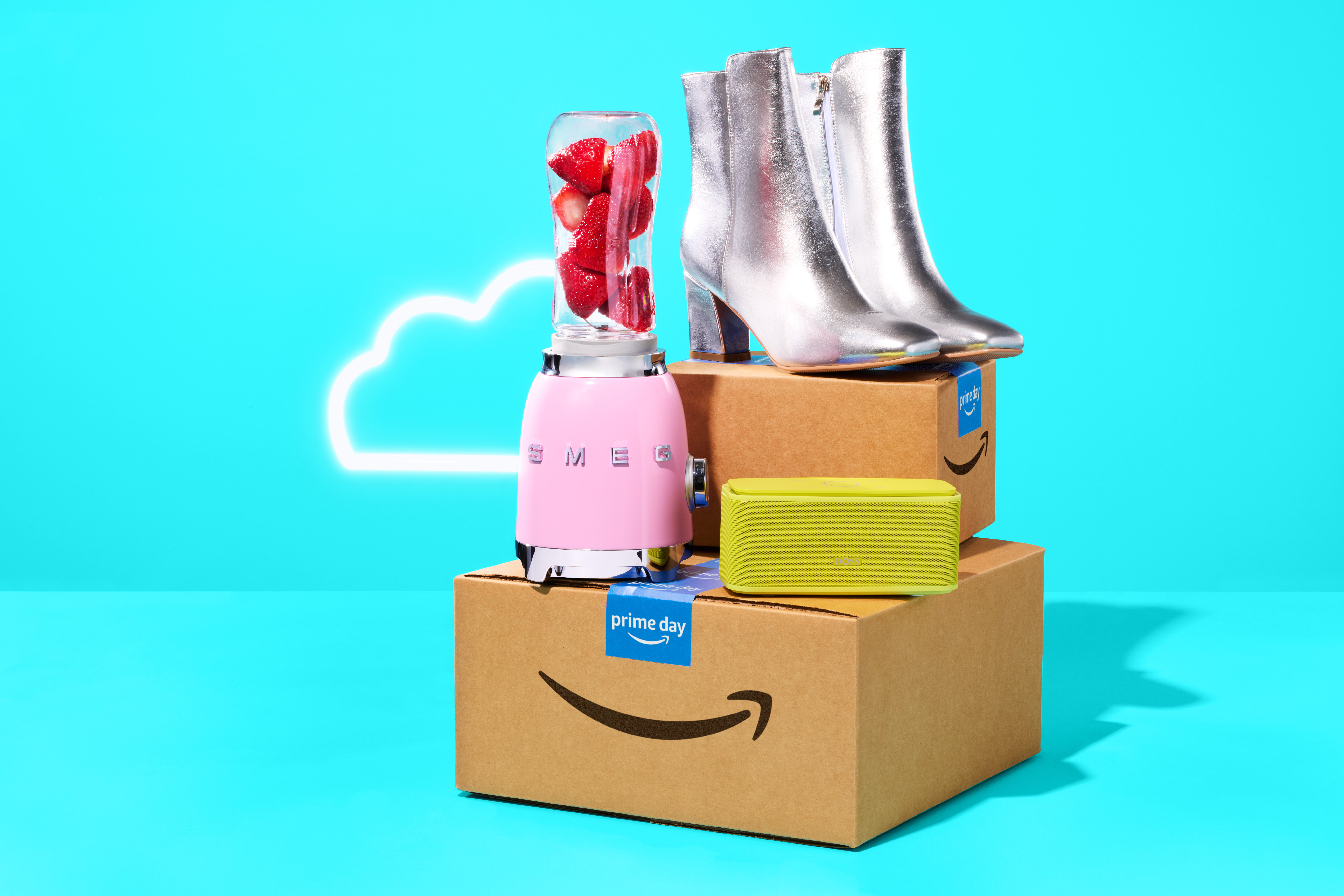 Ein rosafarbener Mixer, silberne Stiefel und grüne Bluetooth-Lautsprecher auf einem Stapel von Amazon-Kartons