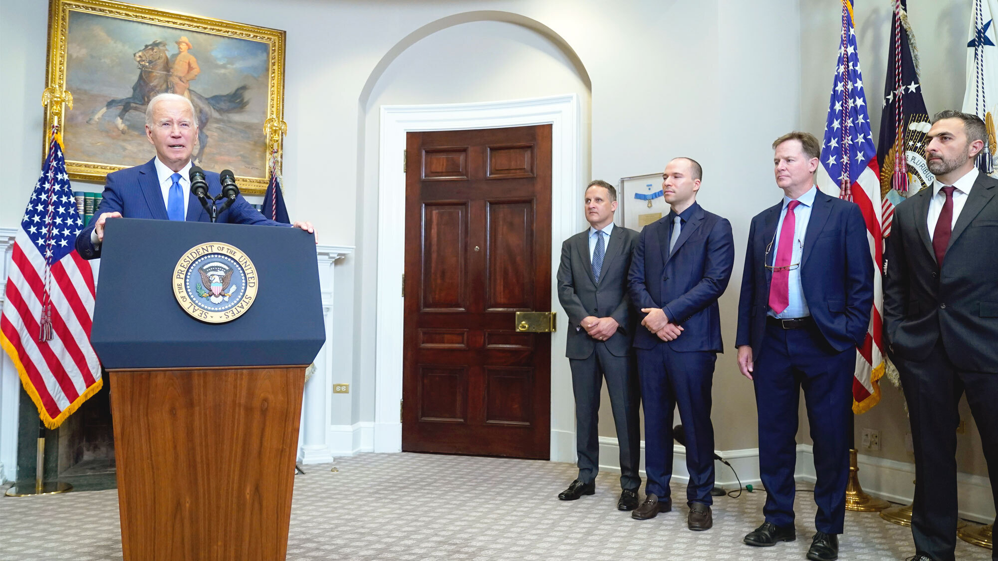 A photo of President Joe Biden speaking at a White House podium with several AI technical leads.