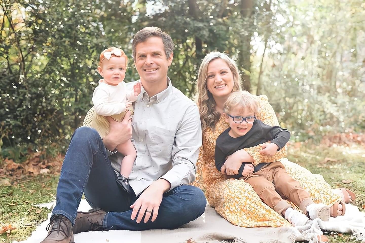 An image of a family sitting for a photo outside in a green area.