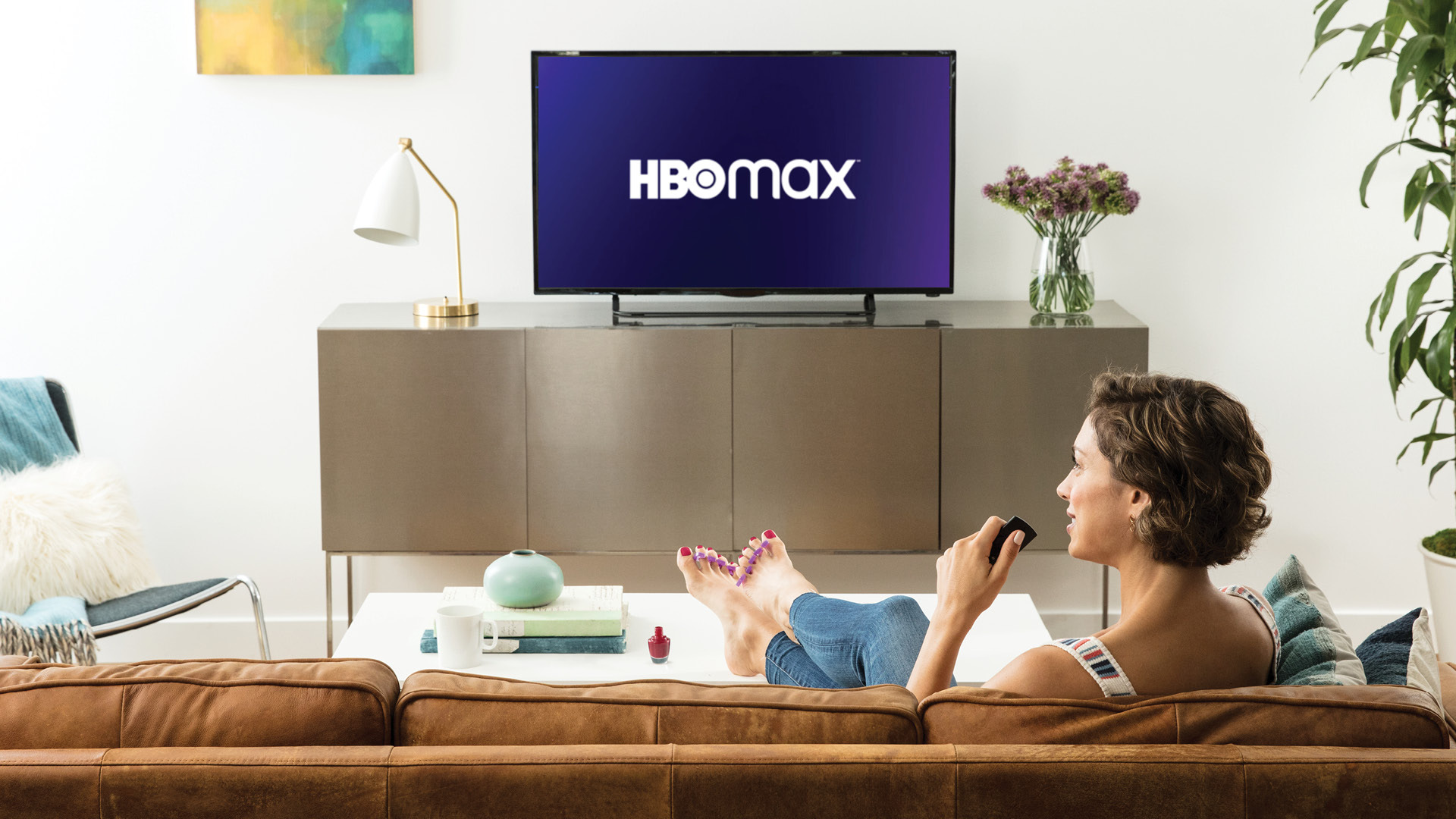 Someone sitting on the couch watching a TV displaying the HBO Max logo.