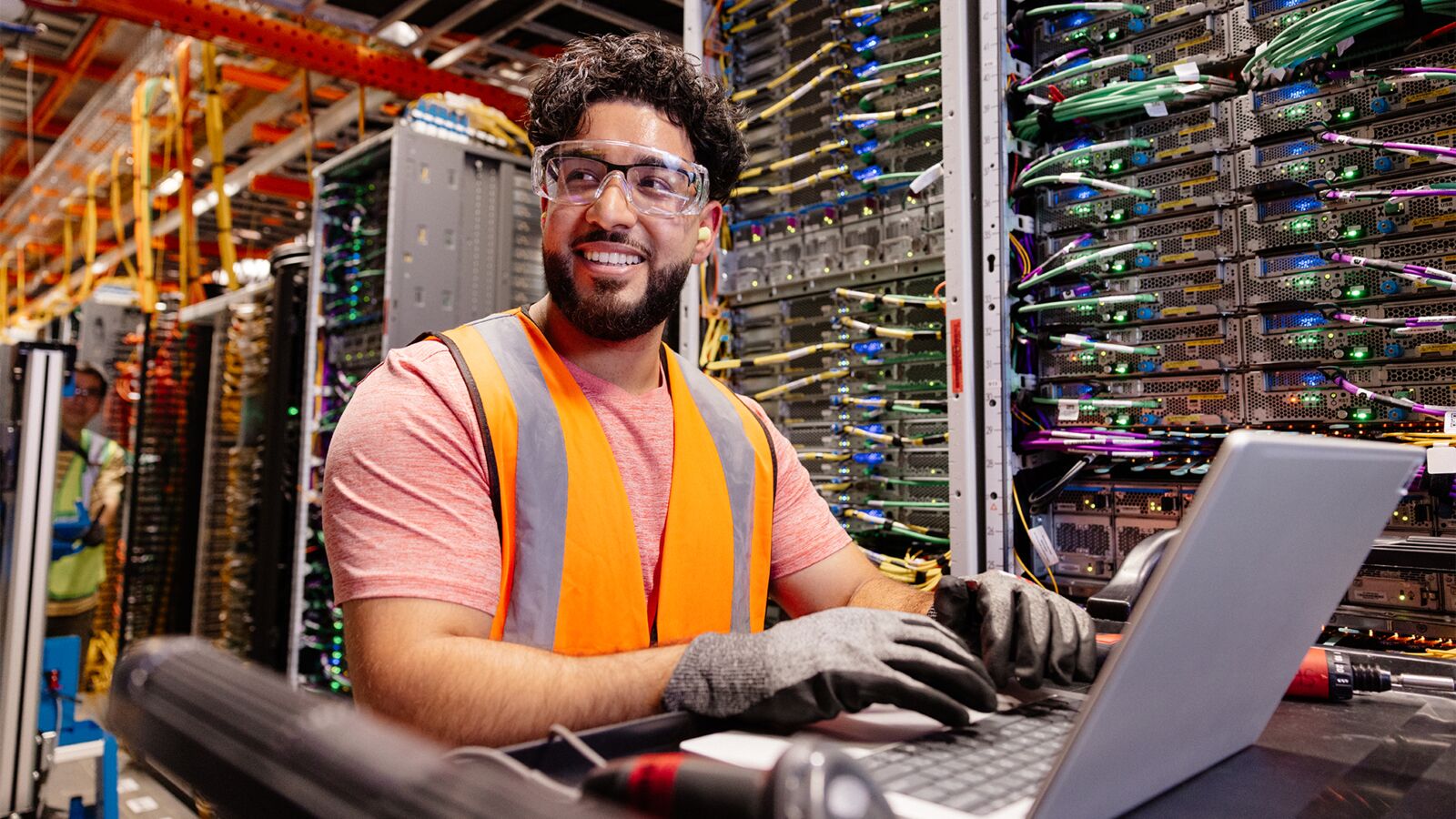 An Amazon employee wears safety gear and works on a laptop at a data center.
