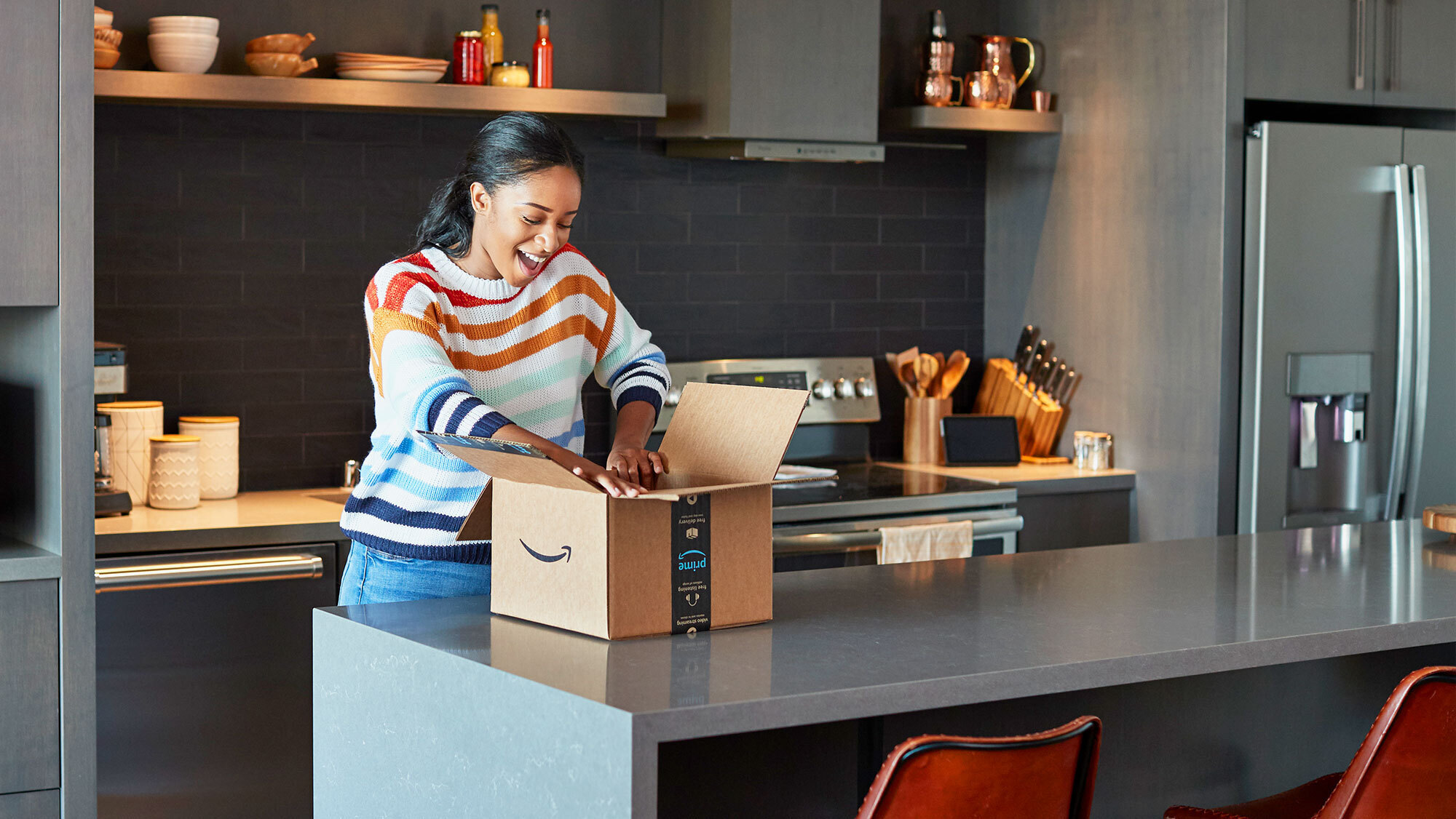 A woman is very excited as she opens an Amazon package in her kitchen.