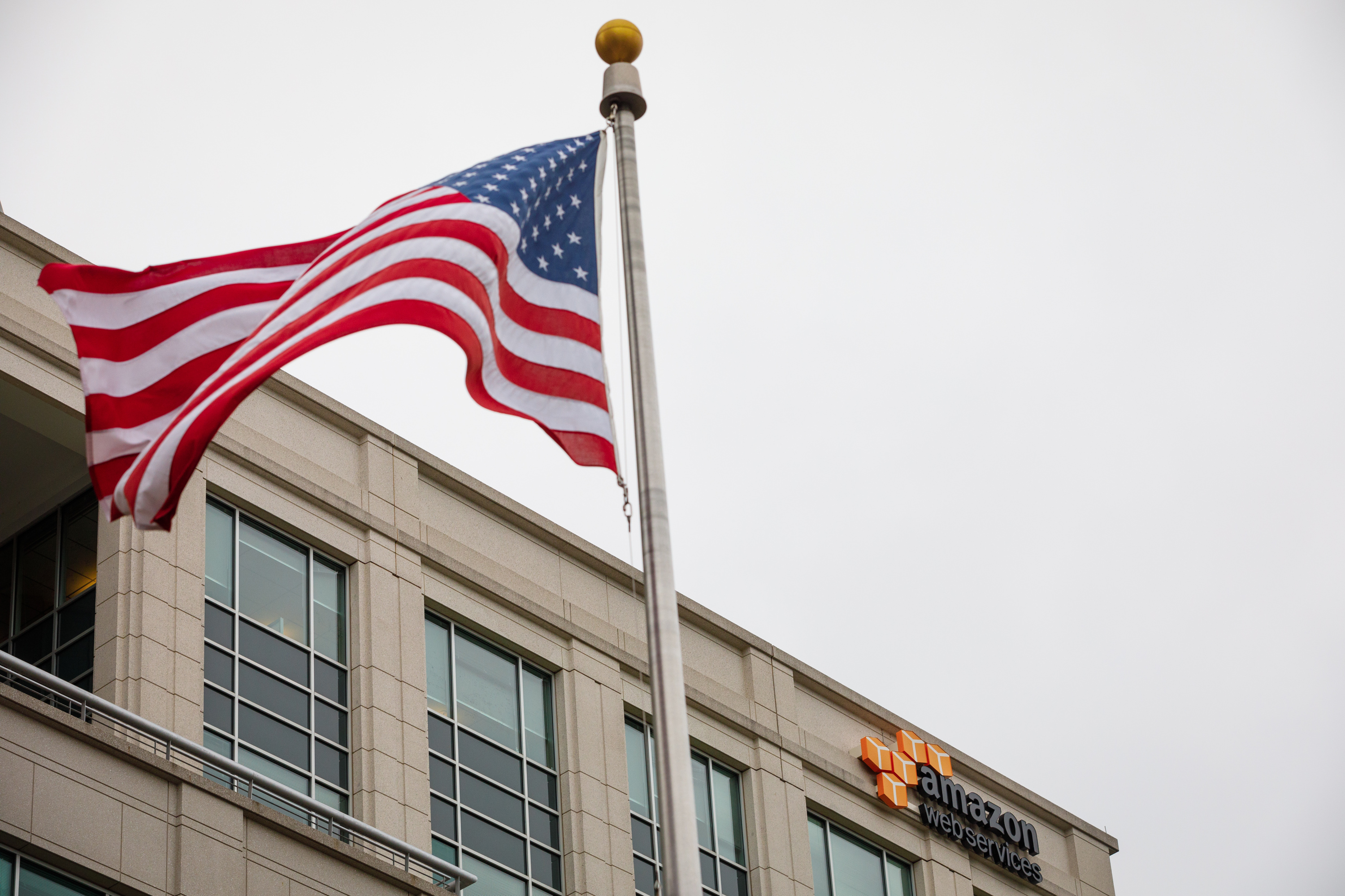 The United States flag moves in the wind in front of an Amazon Web Services building. 