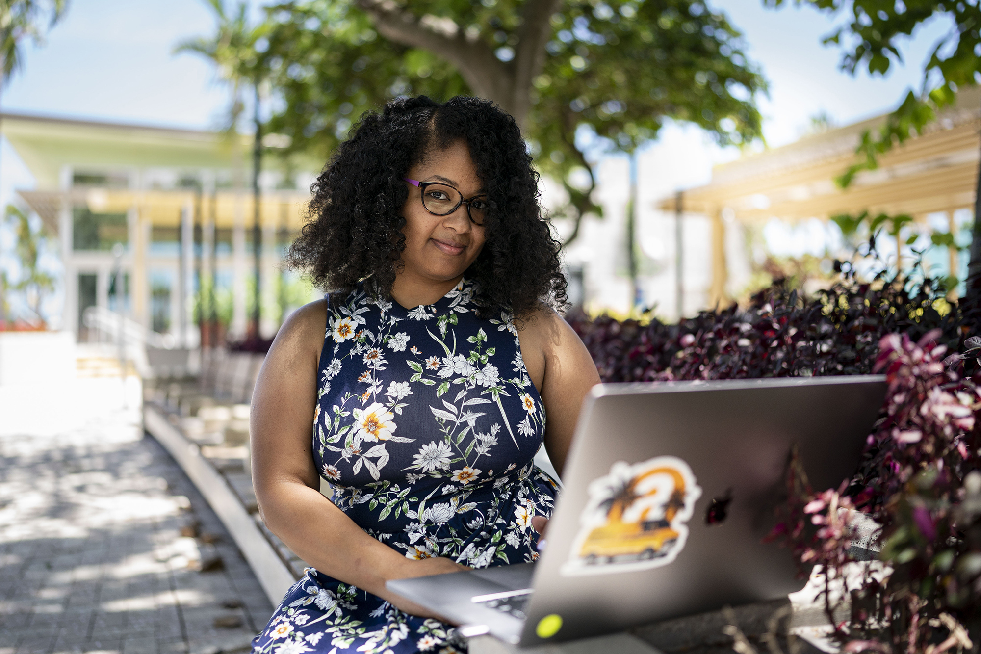 A woman works on a computer in an outdoor setting. She smiles at the camera.