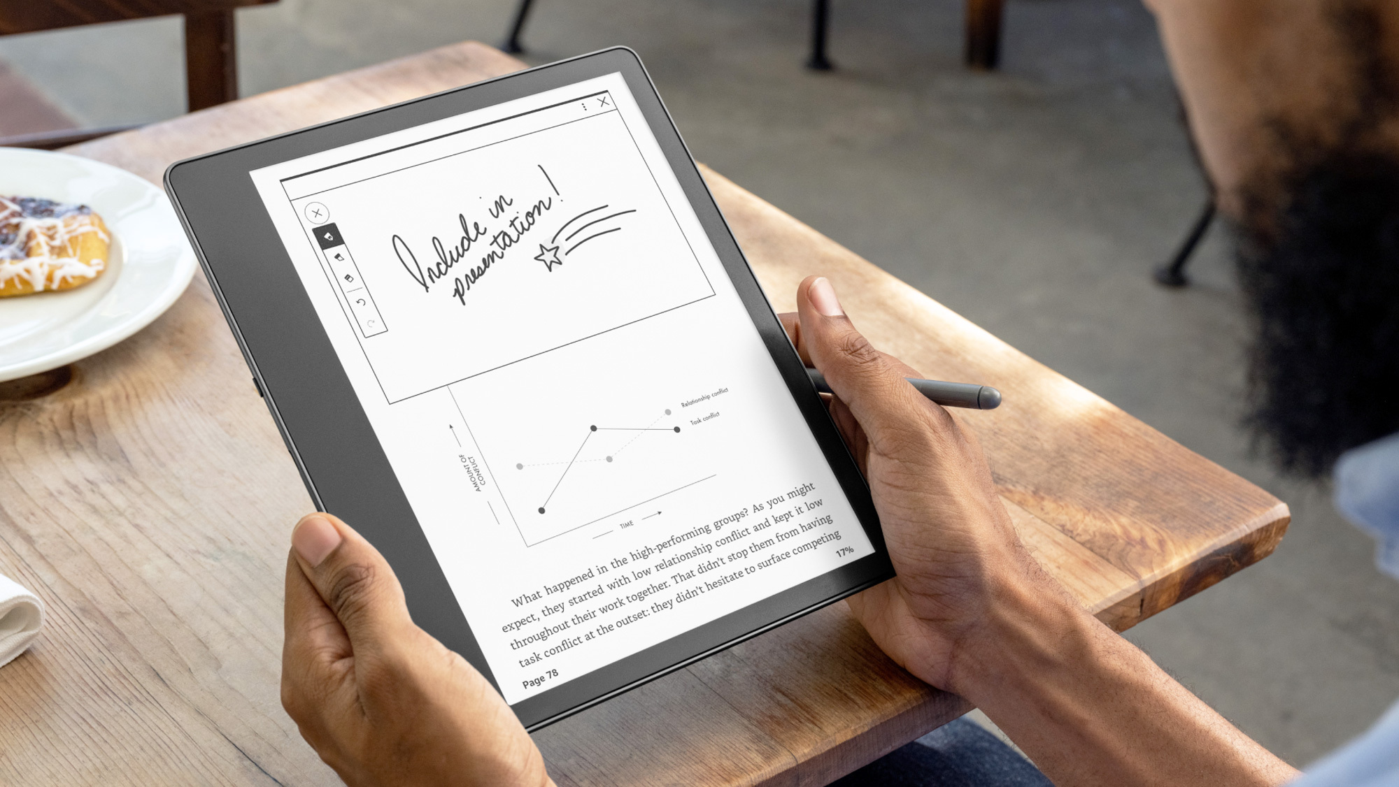 An image of two hands holding the Kindle Scribe on a wooden table.