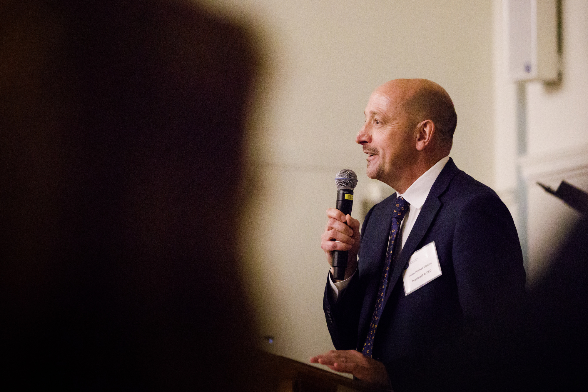 Friendship Place President and CEO  Jean-Michel Giraud speaks through a mic to an event crowd