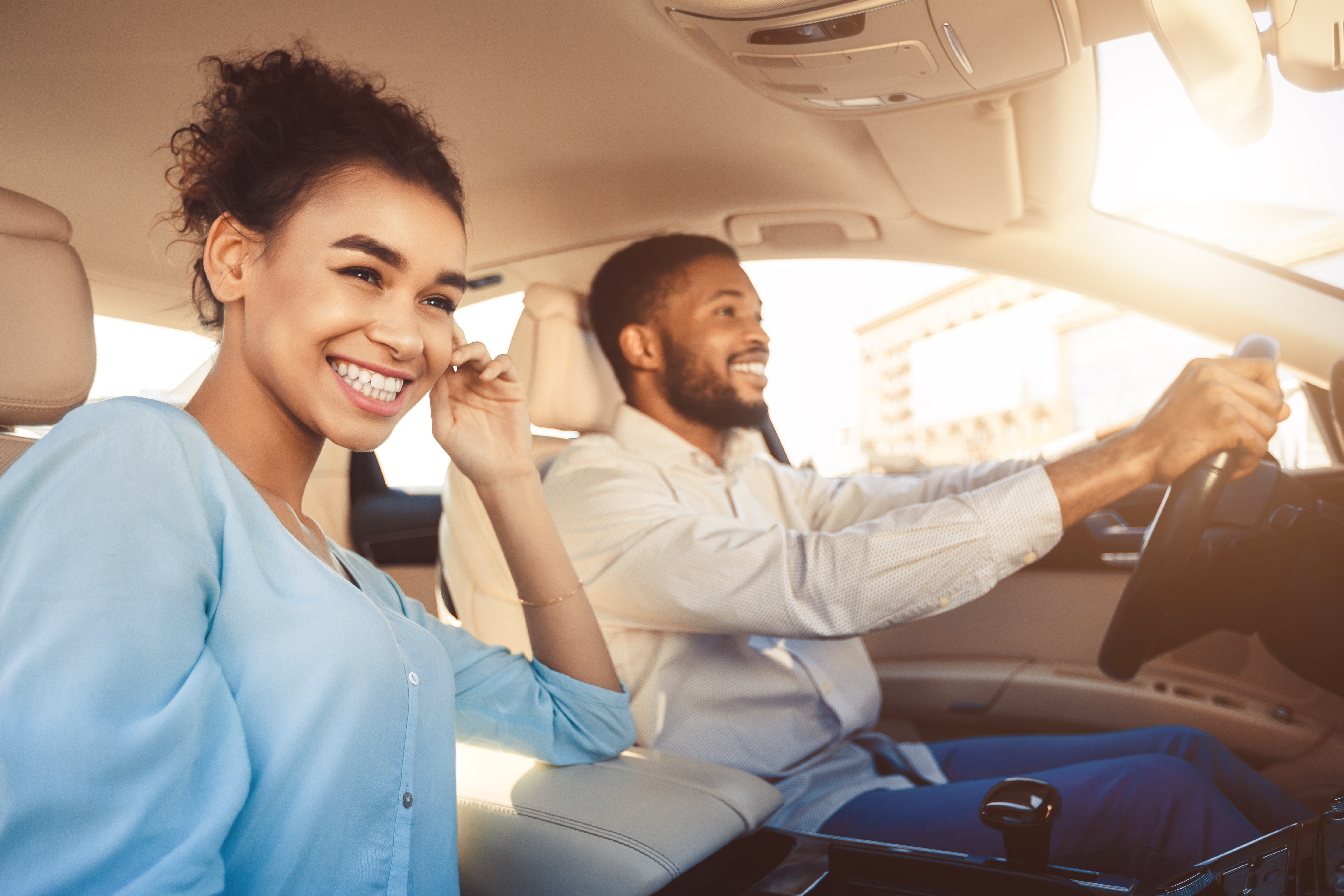 Ein Mann und eine Frau sitzen in einem Auto und lachen. Der Mann sitzt am Steuern und fährt den Wagen.