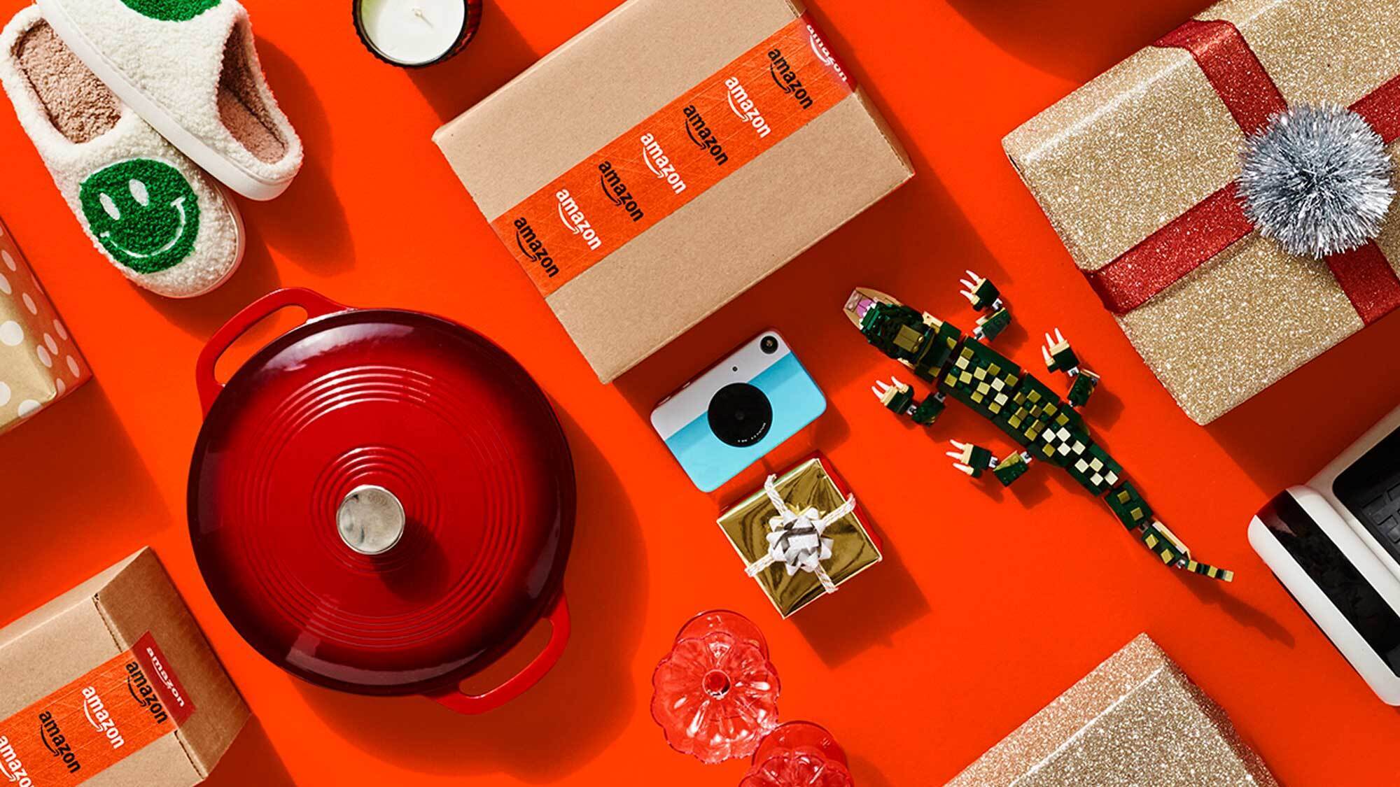 A collection of shipping boxes with Amazon labels, gift-wrapped presents, and unwrapped gifts decoratively placed on a red background. 