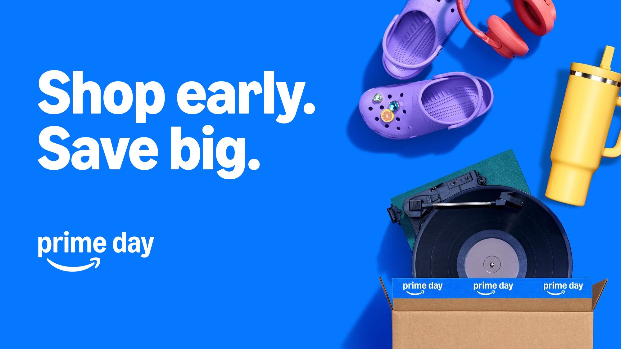 Amazon Prime Day promotional banner with purple Crocs, headphones, tumbler, and tape measure in cardboard box on blue background
