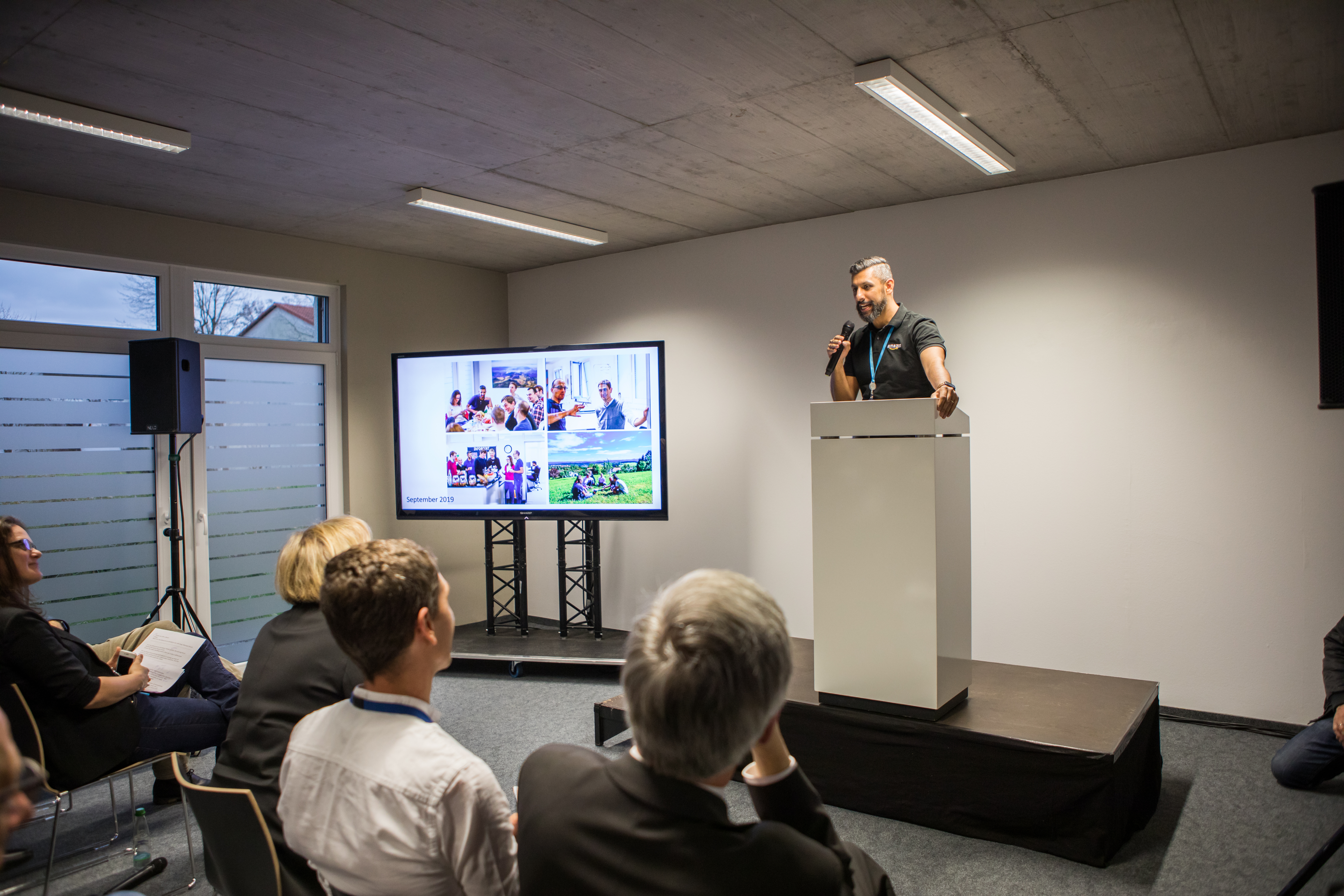 Beim Open House in Tübingen wurden verschiede Vorträge gehalten. Die Gäste sitzen auf Stühlen und schauen sich die Präsentationen auf einem Bildschirm ein.