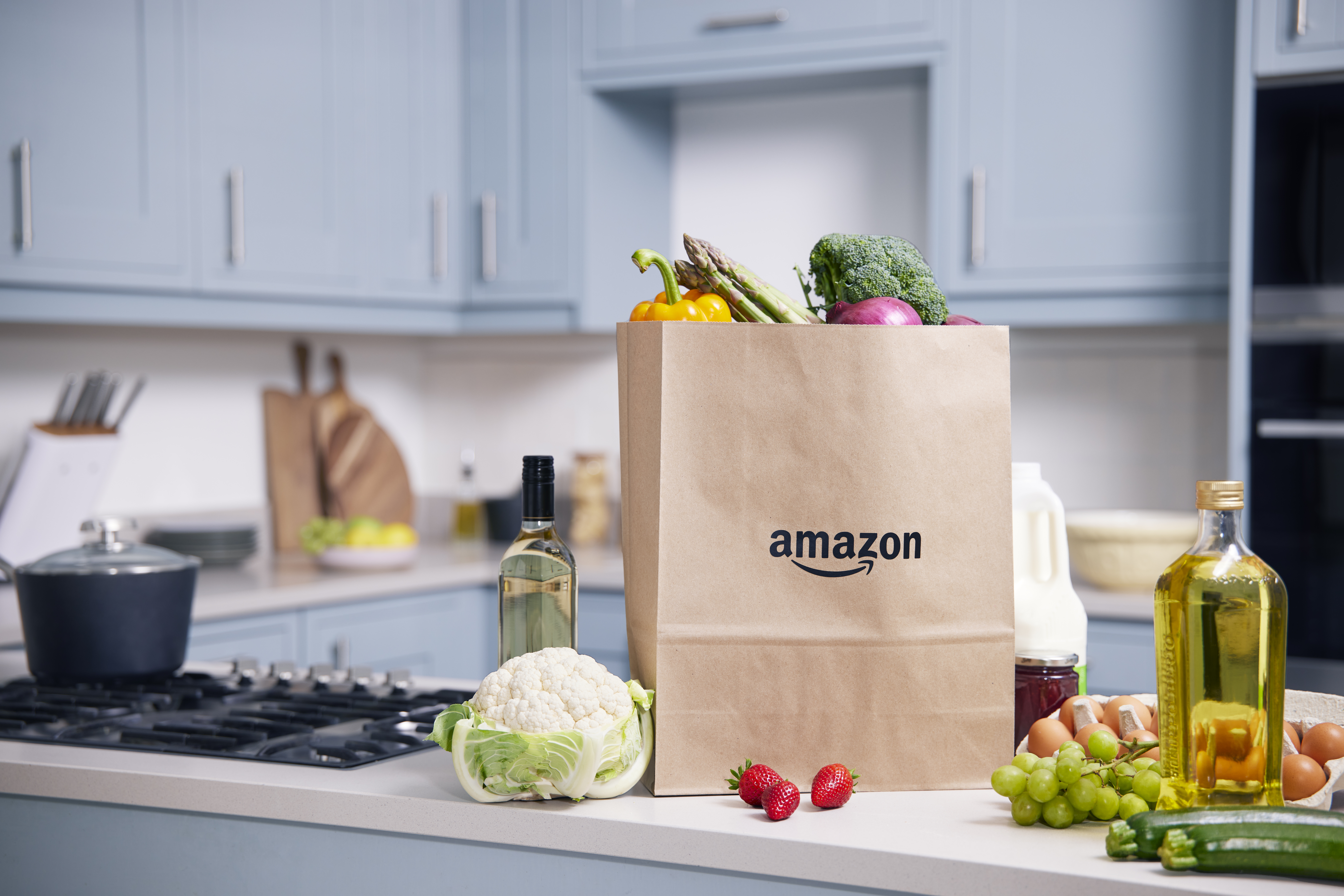 A kitchen counter top with fresh produces like strawberries, cucumber, grapes, eggs and a paper bag with the amazon label on it