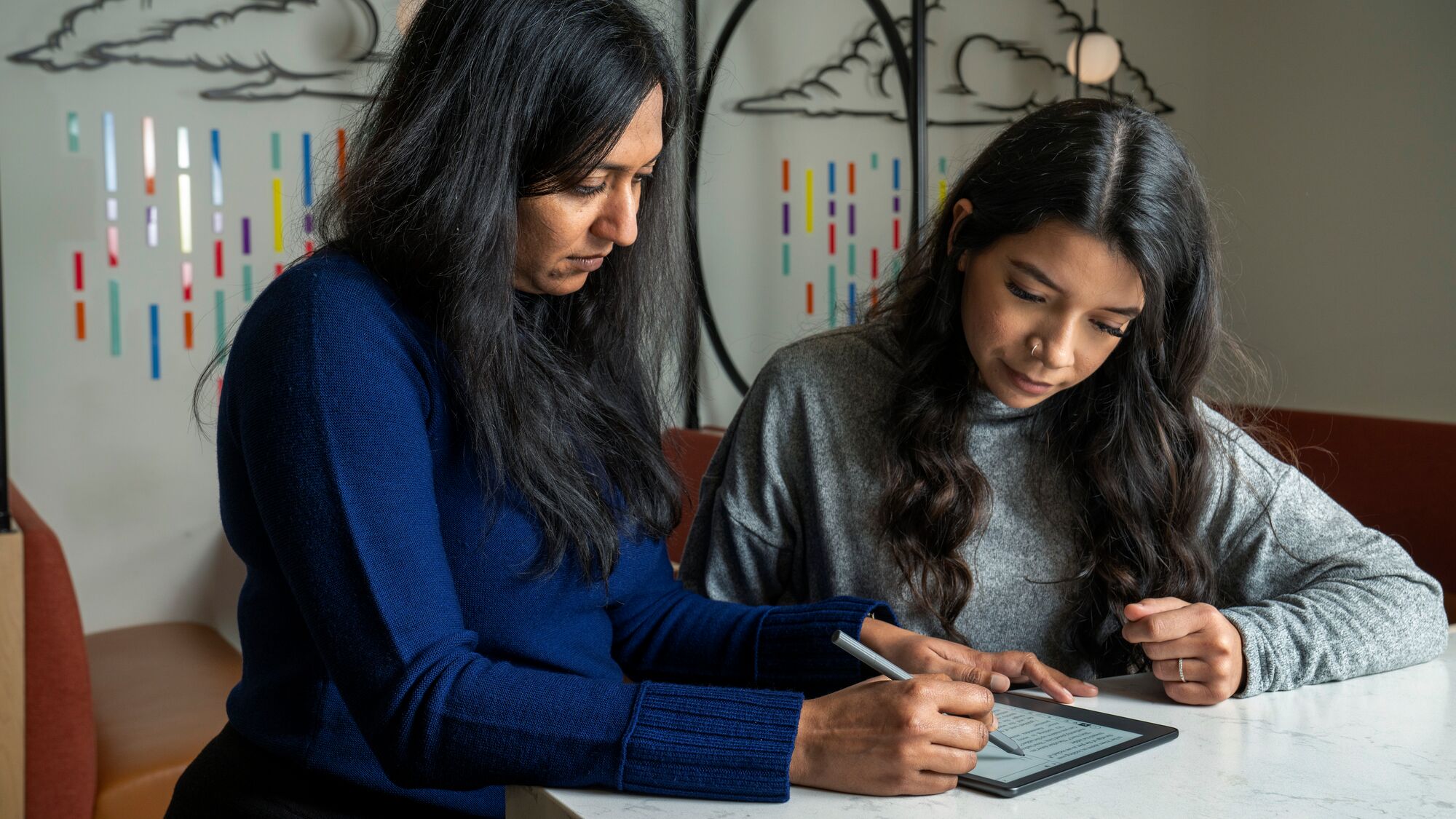 Two women focused on digital tablet, learning together