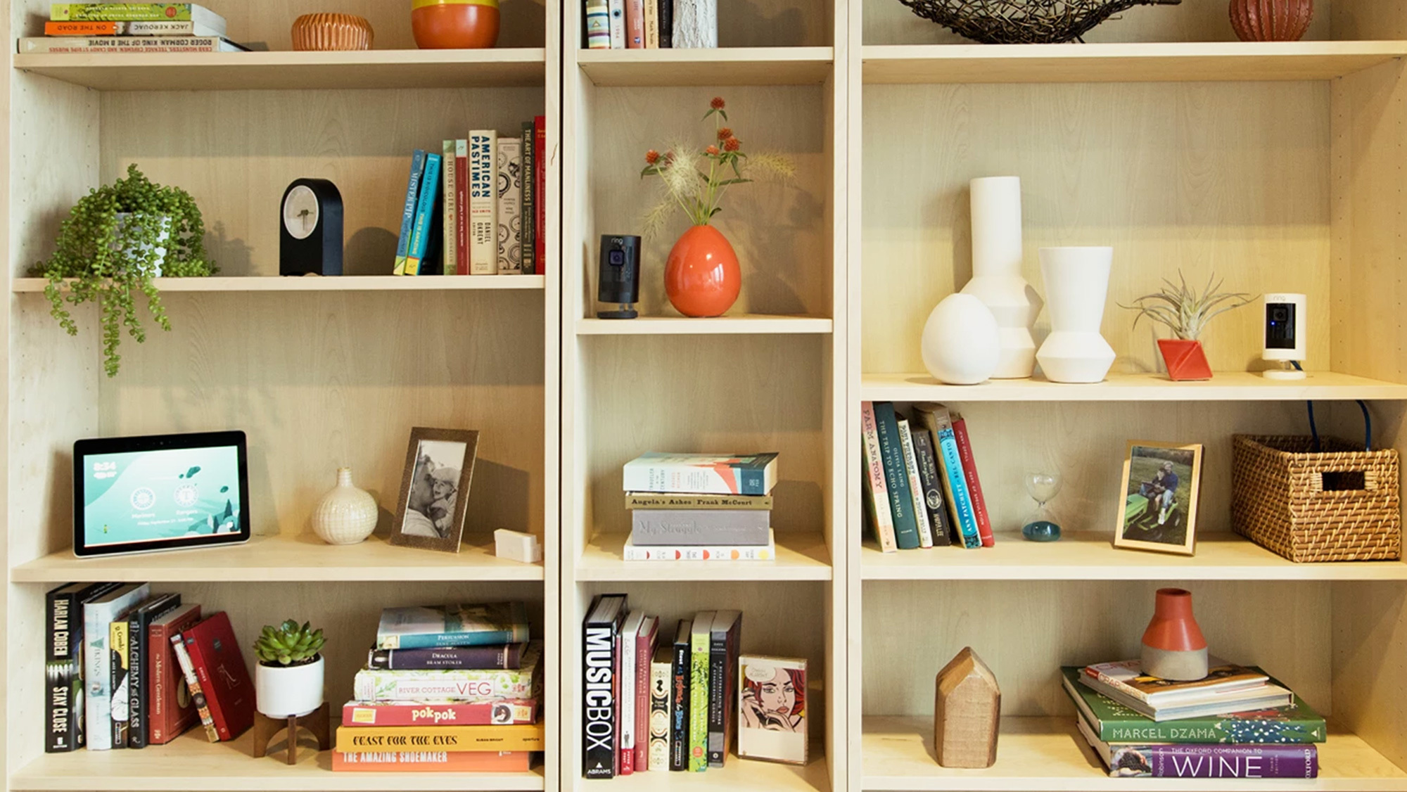 A shelf filled with books, vases, decor, and smart home devices.