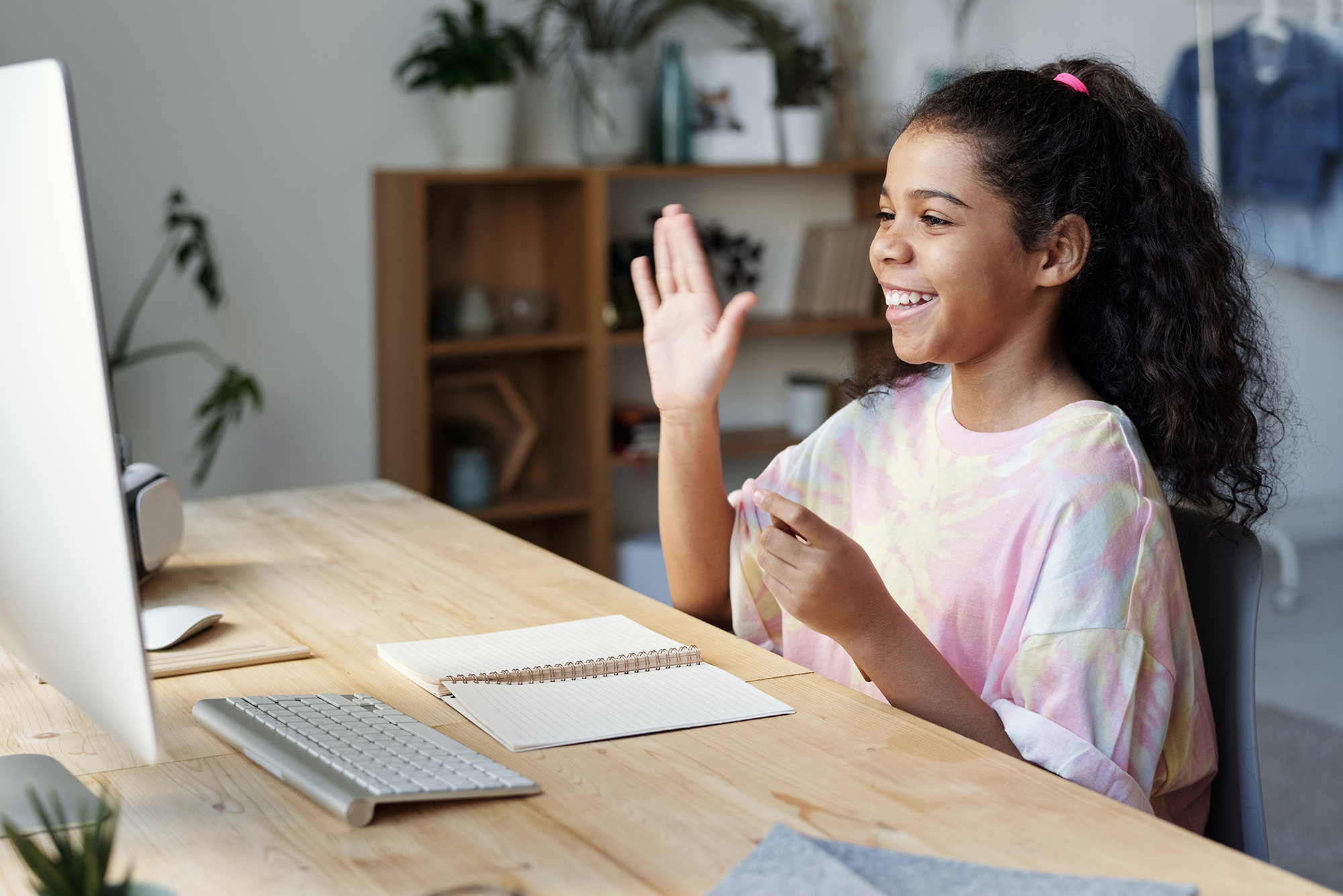 A young woman waves at her computer monitor as sheparticipates in a video chat. 