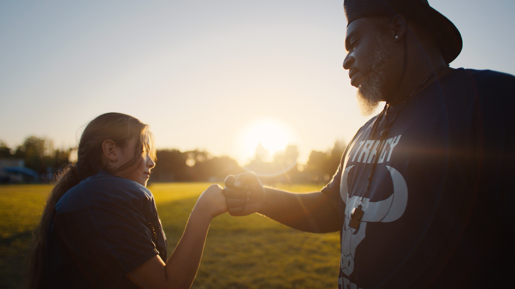 A football coach and a player fist bump. The player is a female little league player.