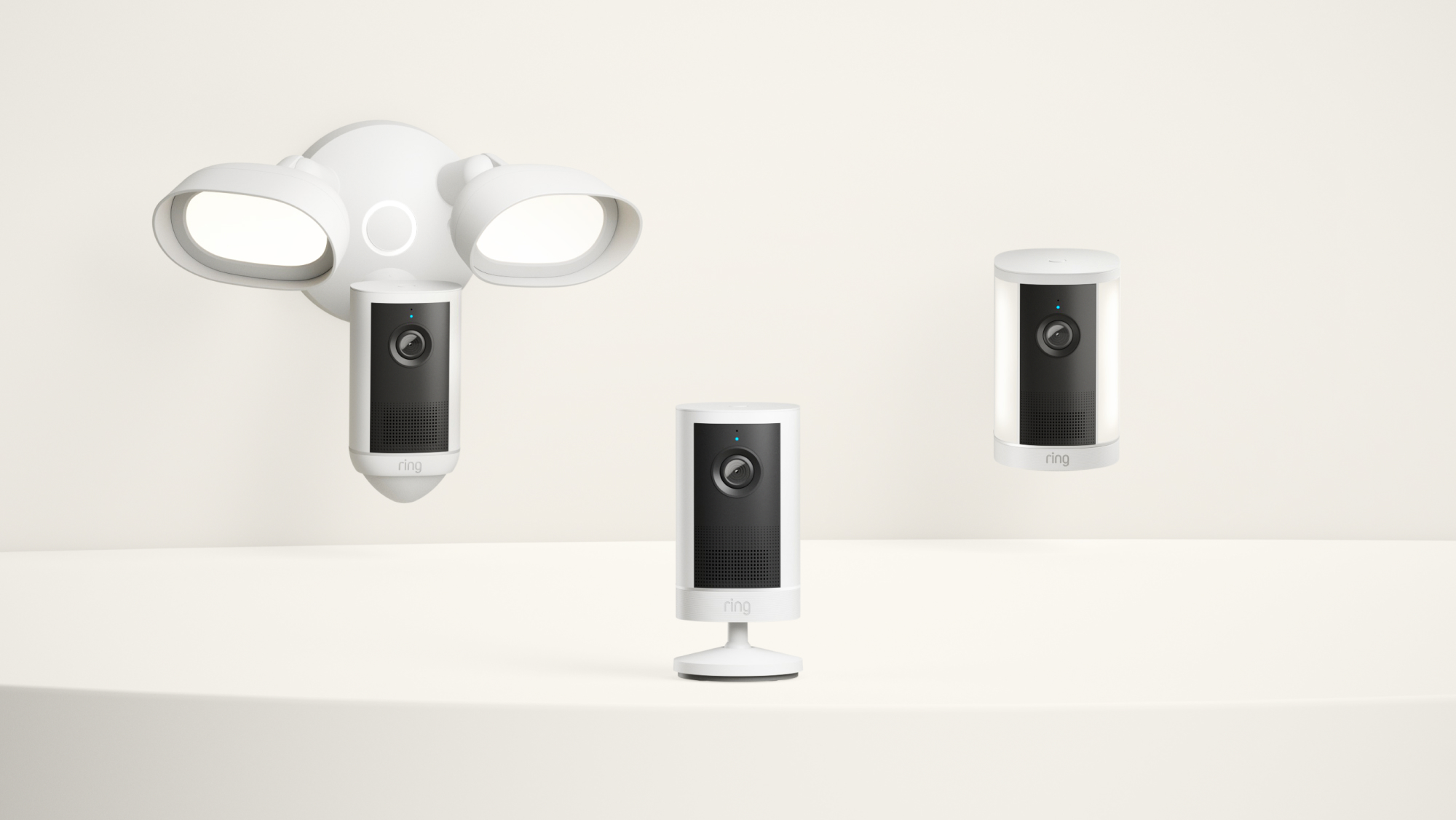 Three Ring security cameras in a lineup: floodlight cam, stick-up cam with mount, and stick-up cam on a flat surface