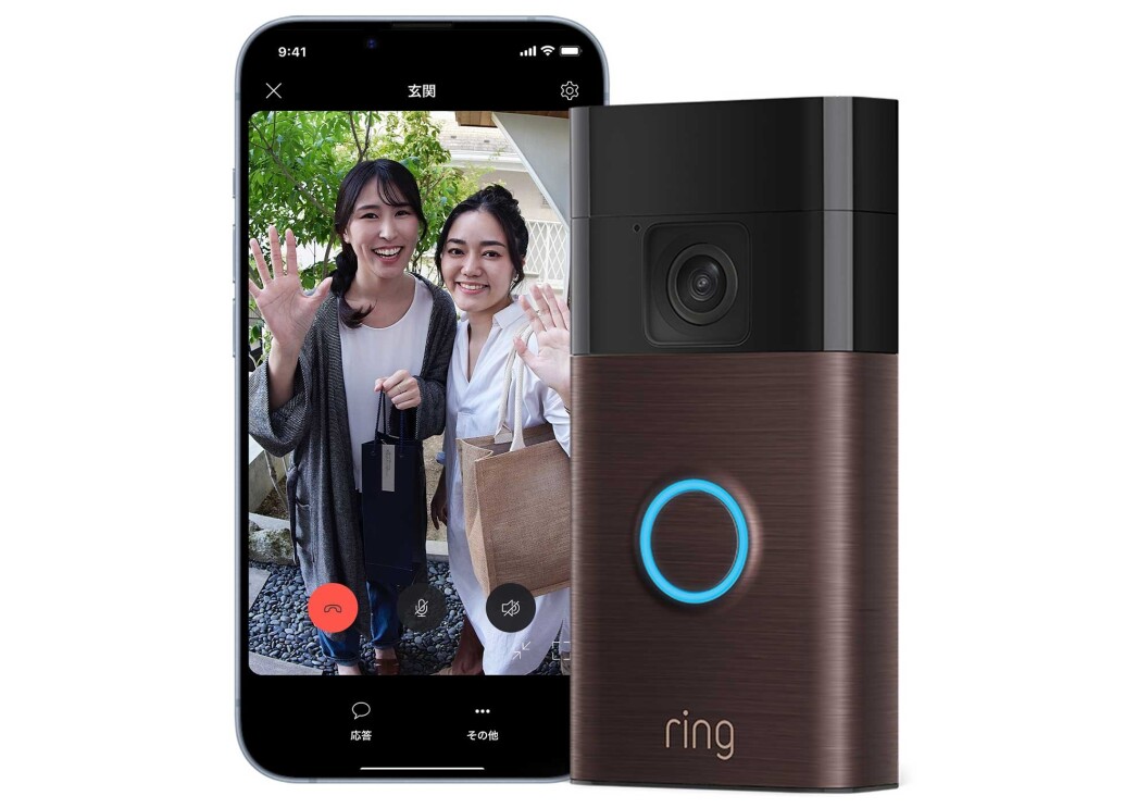 ブロンズ色のRingドアベルの左側にスマートホン。その画面には、カメラに向かって手を振る2人の女性が映っている