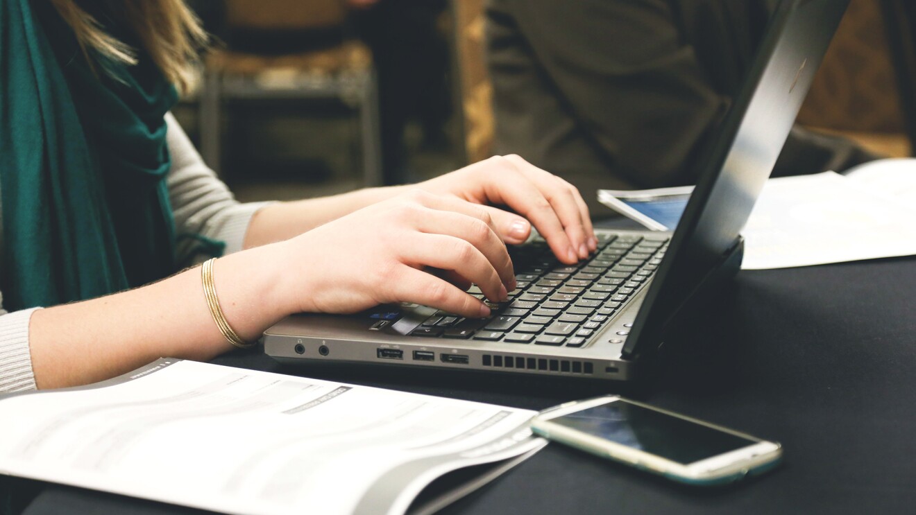 Woman working on a laptop computer, her hands are posed over the keyboard of the device.