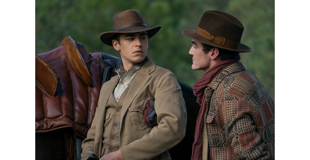 木々の緑を背景に、カウボーイハットをかぶった2人の男性が見つめあう。