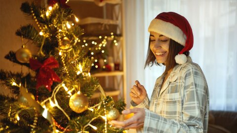 Una mujer con un gorro de papá noel delante de un árbol de Navidad. 