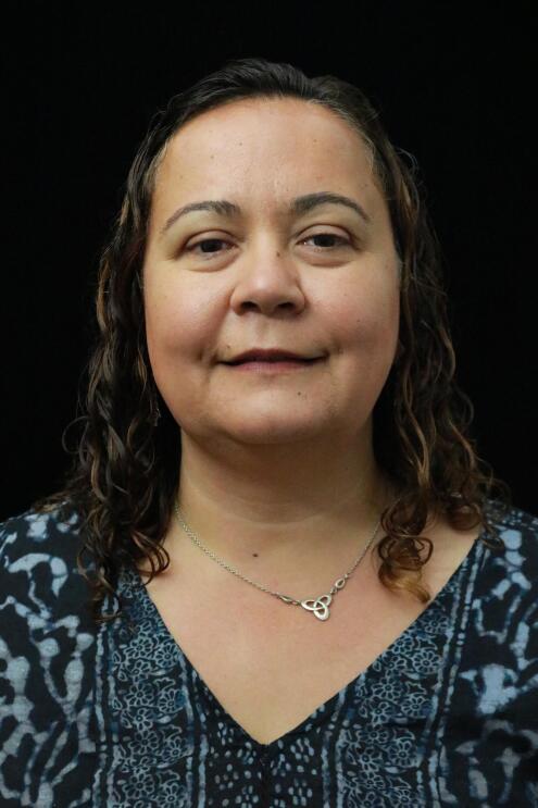 Dilek Hakkani-Tür, a senior principal scientist in the Alexa AI group smiles at the camera. She wears a gray button down shirt and her brown hair is pulled back in a low pony tail.