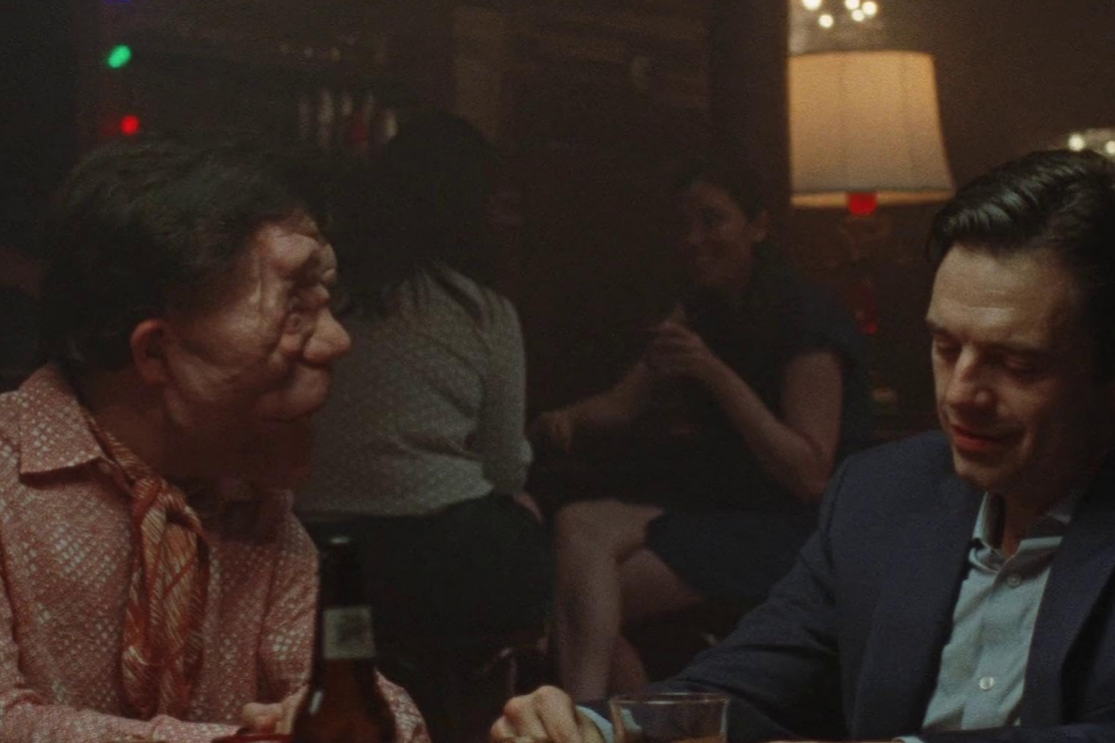 Two characters sit in a bar in a scene from the oscar nominated movie A Different Man