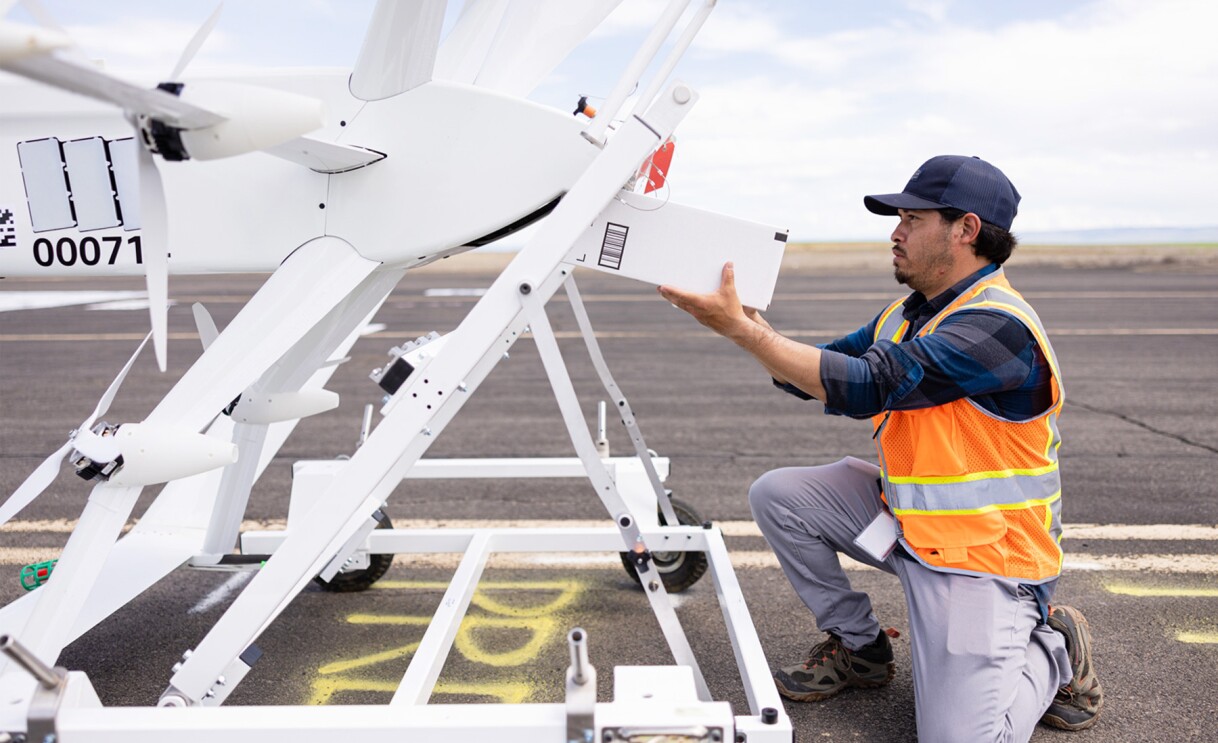 Images of Amazon employees wearing orange safety vests work on drones.