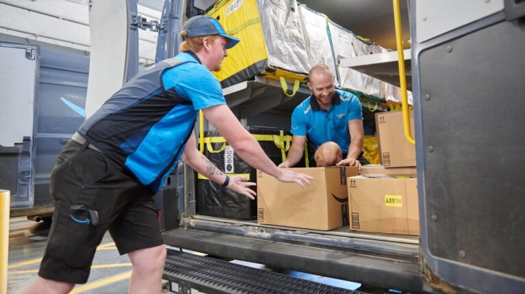 Two Amazon workers smile while loading a delivery van
