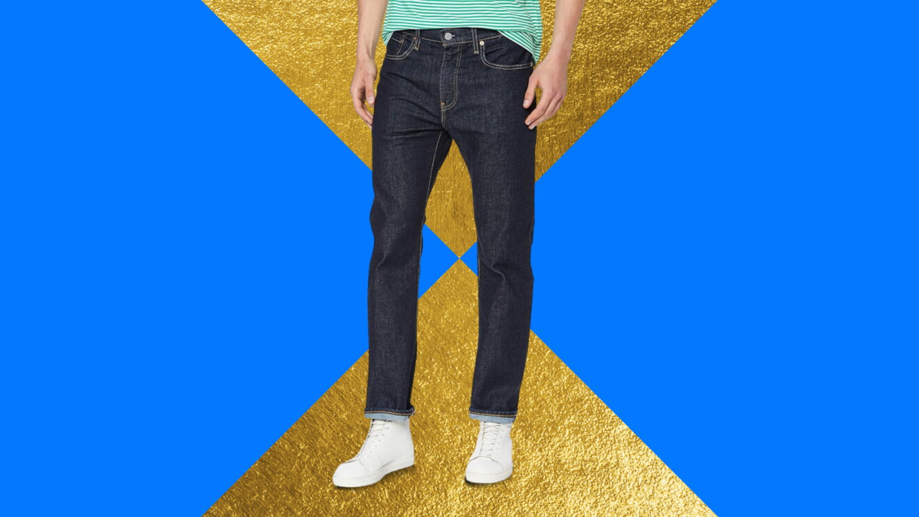 Man wearing dark jeans and white sneakers against blue and gold background
