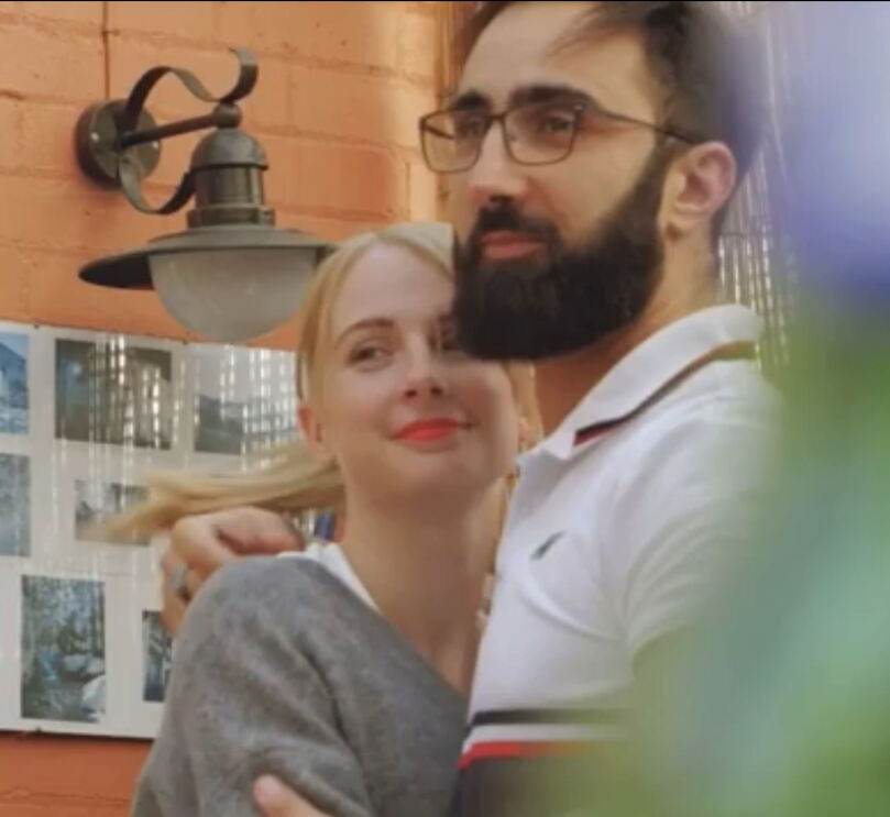 A man and woman embrace, a close up item is blurred in the image. 