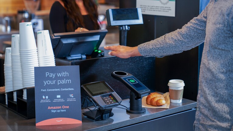 A photo of a customer's arm and hand, which is hovering over an Amazon One scanner to purchase a coffee and croissant with Amazon One.