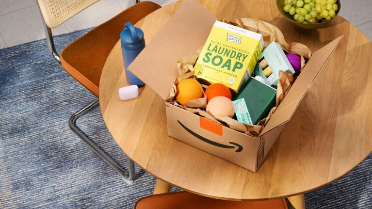 Opened Amazon delivery box with laundry soap, dryer balls, and household products on a wooden table
