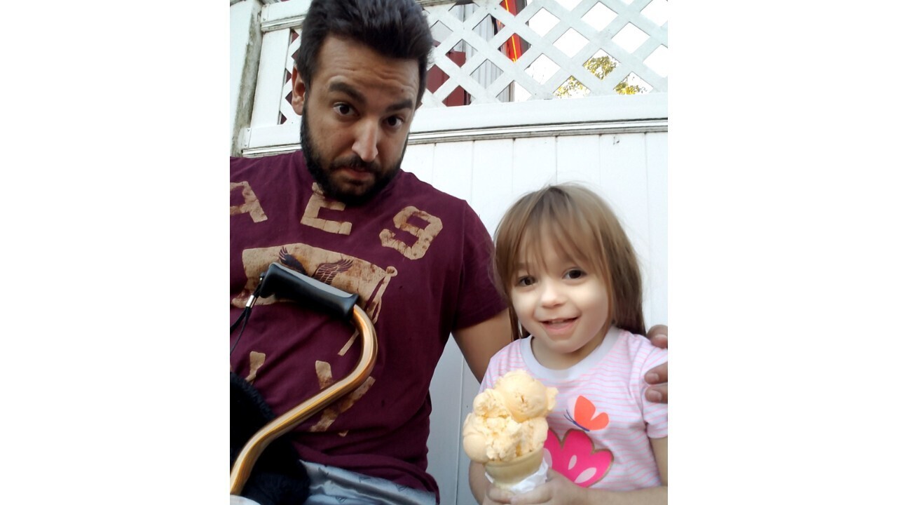 A father sits with a cane in his lap next to his daughter as she holds an ice cream cone.