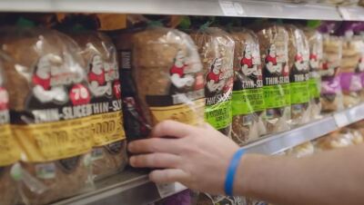 一个人从架子上取下一个包面包在全食超市商店。