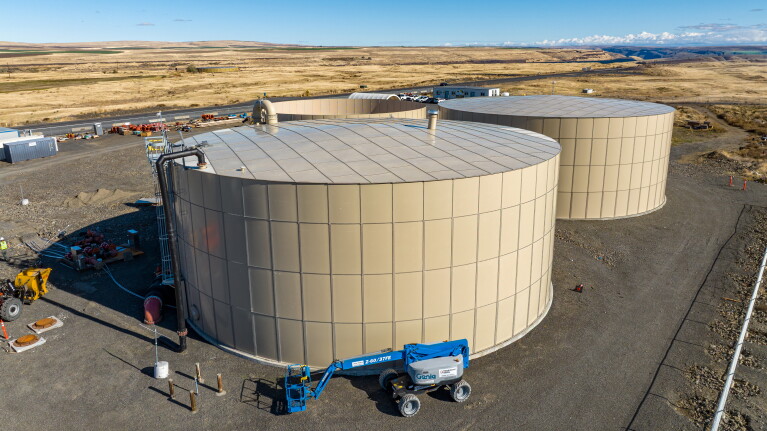 Large cylindrical storage tanks in arid landscape with construction equipment